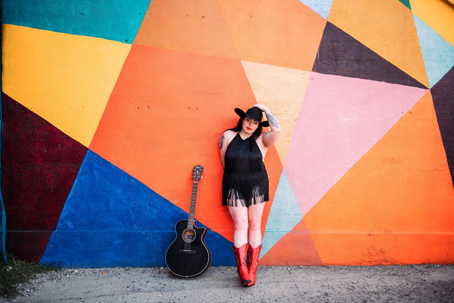 Feet in colorful boots stand against a vibrant geometric wall mural painted in orange, blue and pink shapes.