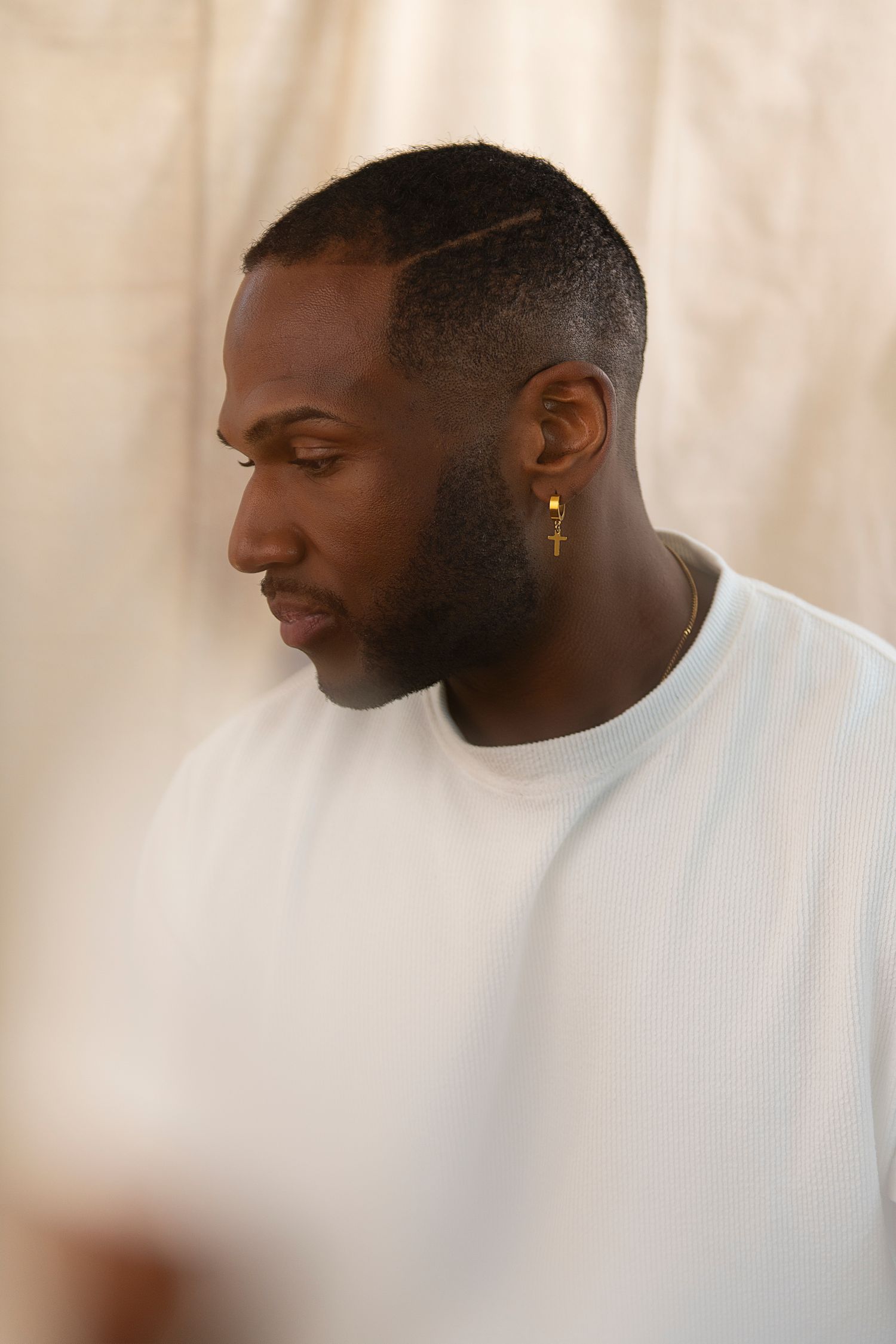 A person wearing a white shirt and gold earring looks to the side in a profile view against a light background.