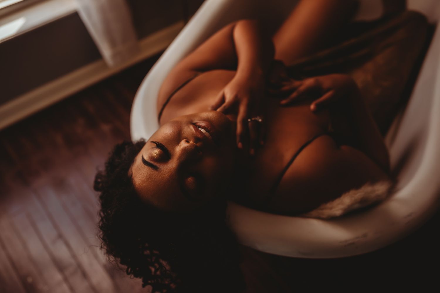 Intimate boudoir photography with soft natural window lighting creating gentle shadows.