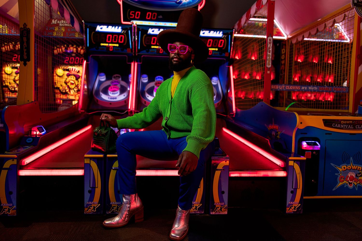 Person in green hoodie sits on neon-lit steps in an arcade-style environment with vibrant pink lighting.