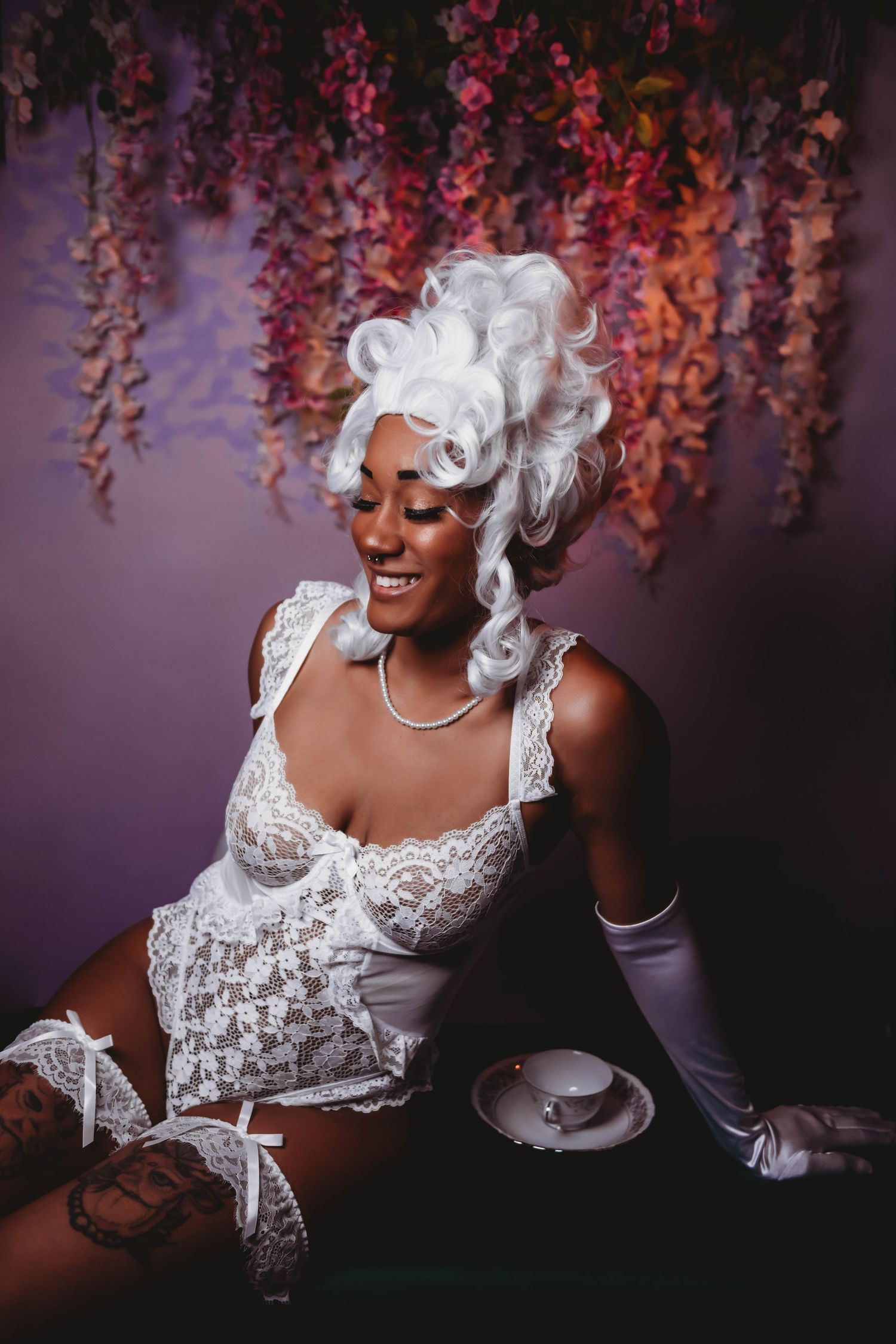 Dramatic portrait in white lace costume with flowing fabric against hanging flowers.