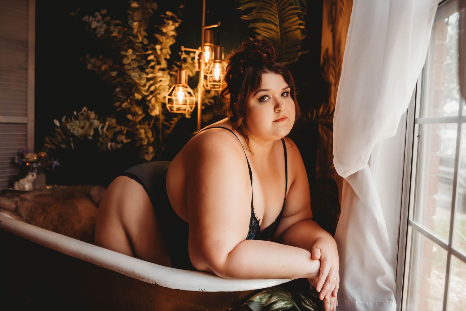 Artistic boudoir session near window with natural light and romantic ambiance.