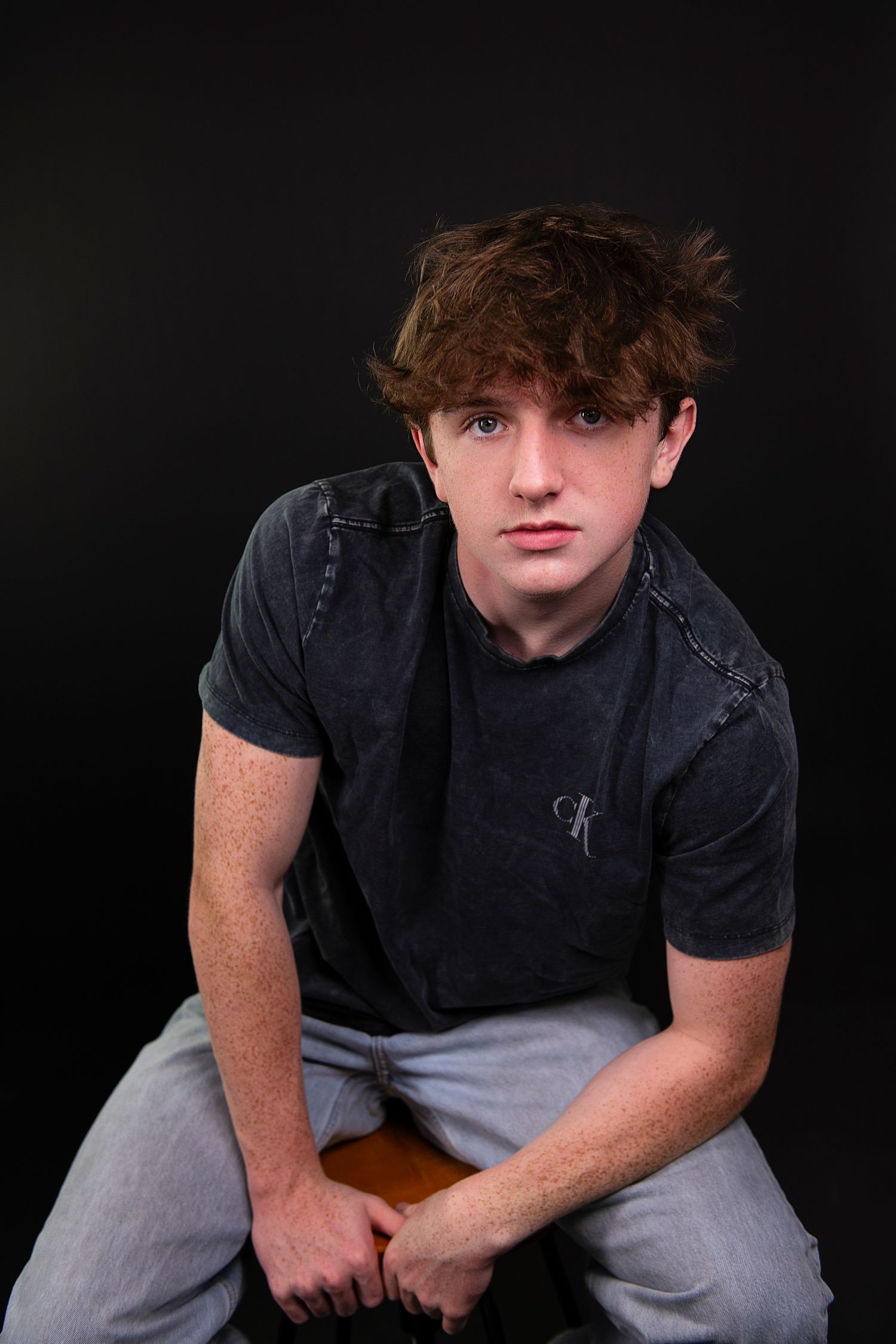 Person wearing black t-shirt and gray pants poses against dark background in four similar portrait shots.