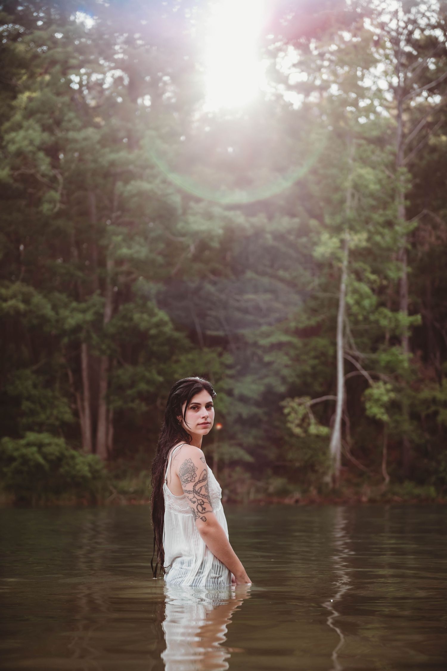 Dreamy outdoor water portrait with sunlit forest backdrop.