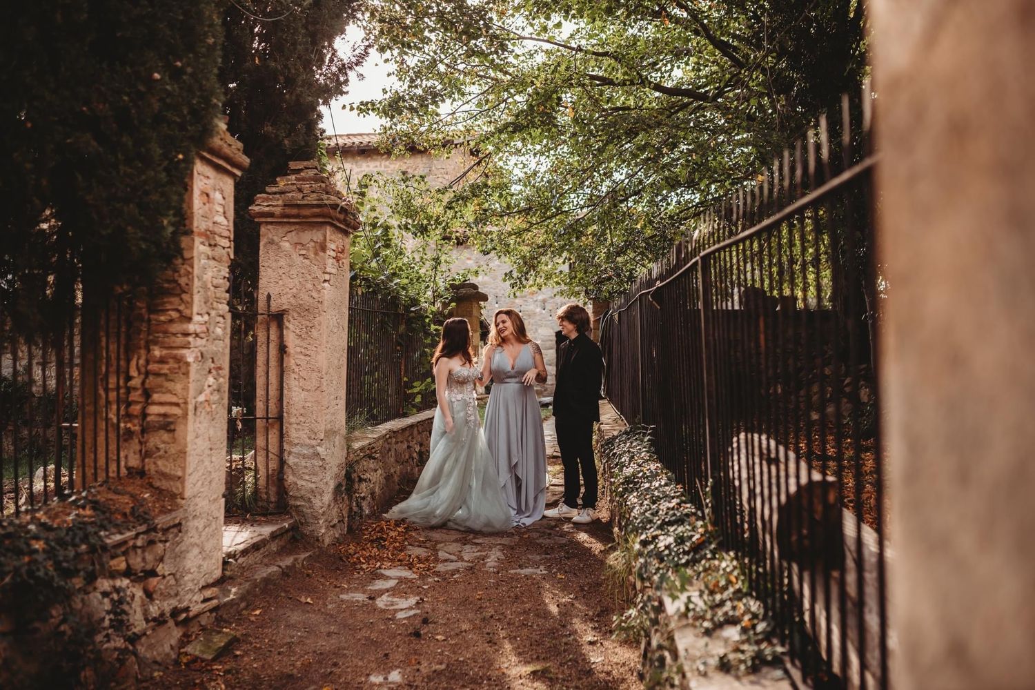 Stone walkway surrounded by lush greenery and iron gates creating romantic wedding scene.