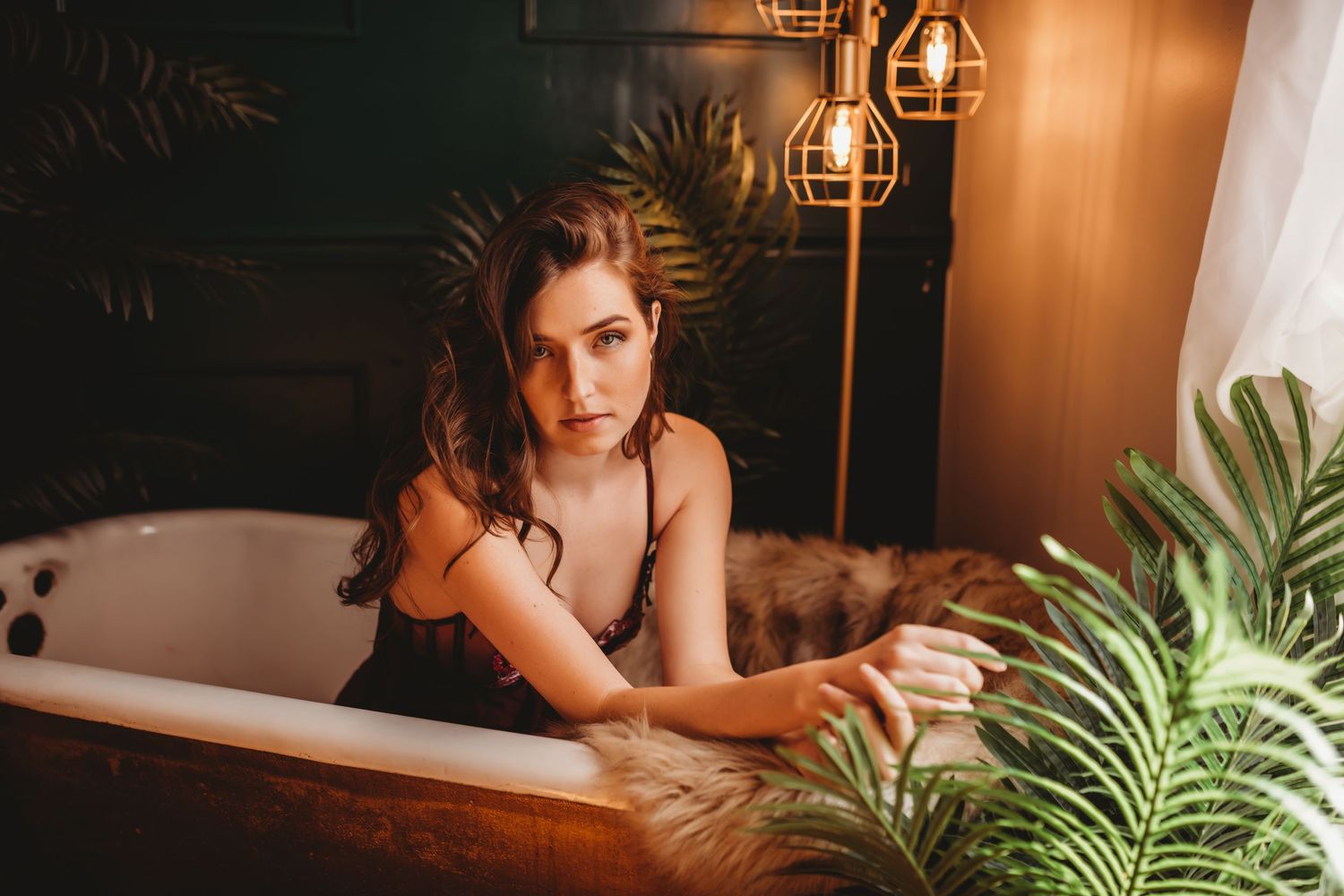 Woman relaxing at home in warm evening lighting with tropical plants and lanterns creating cozy atmosphere.