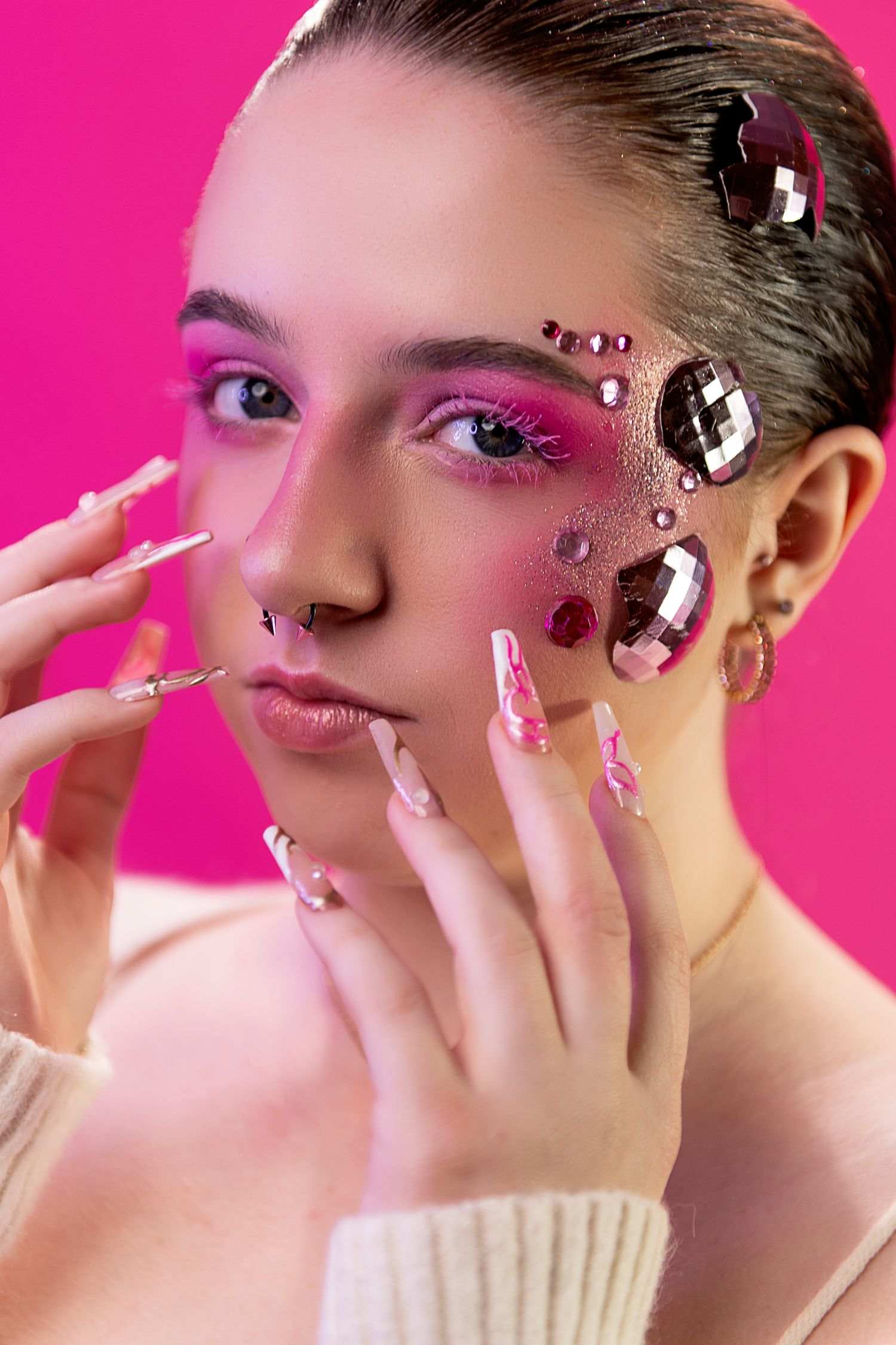 Creative beauty portrait with bright pink eyeshadow, crystal face decorations and long artistic manicure against pink background.