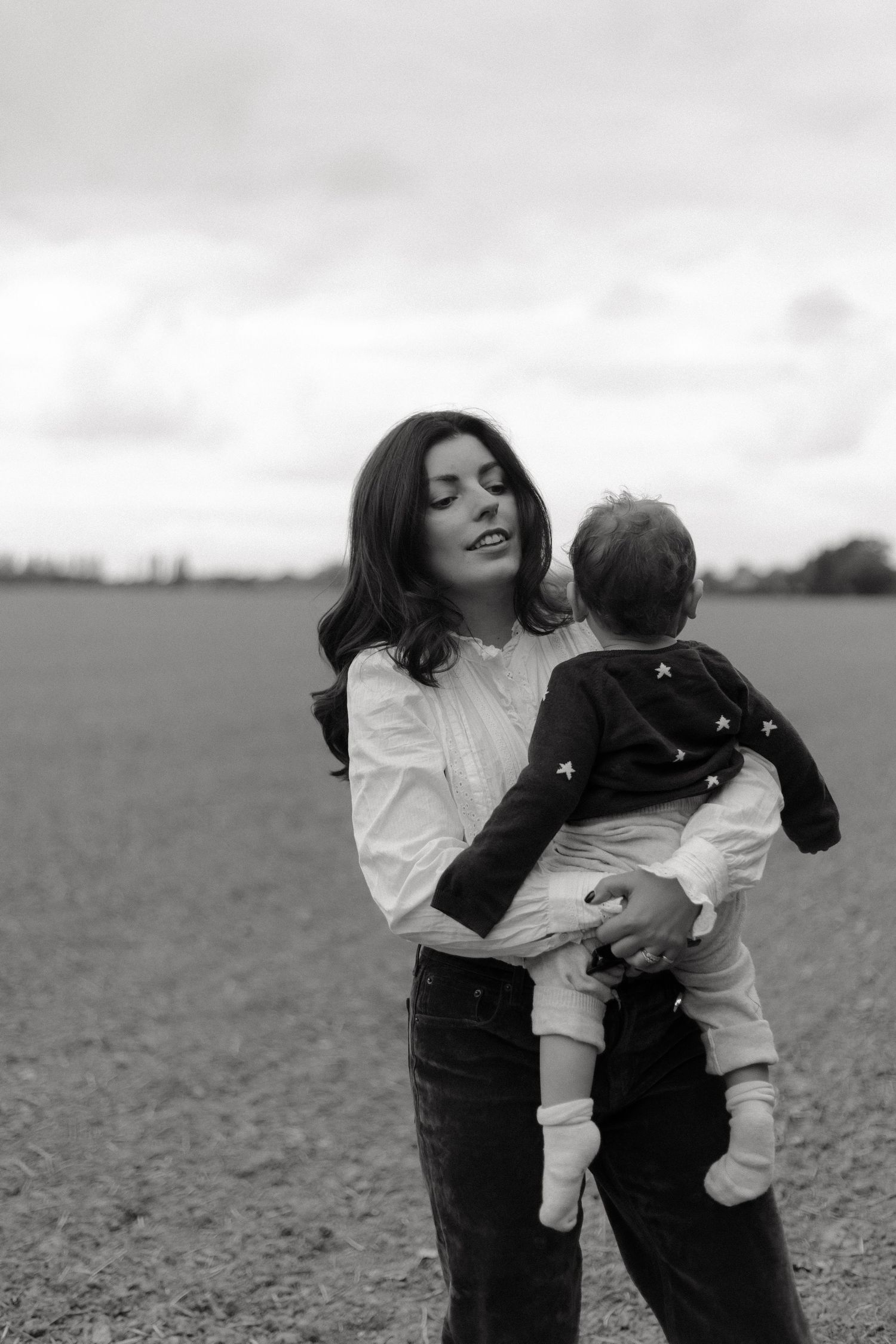 black and white photo of a woman holding her 13 month old son and looking in the distance as he faces her