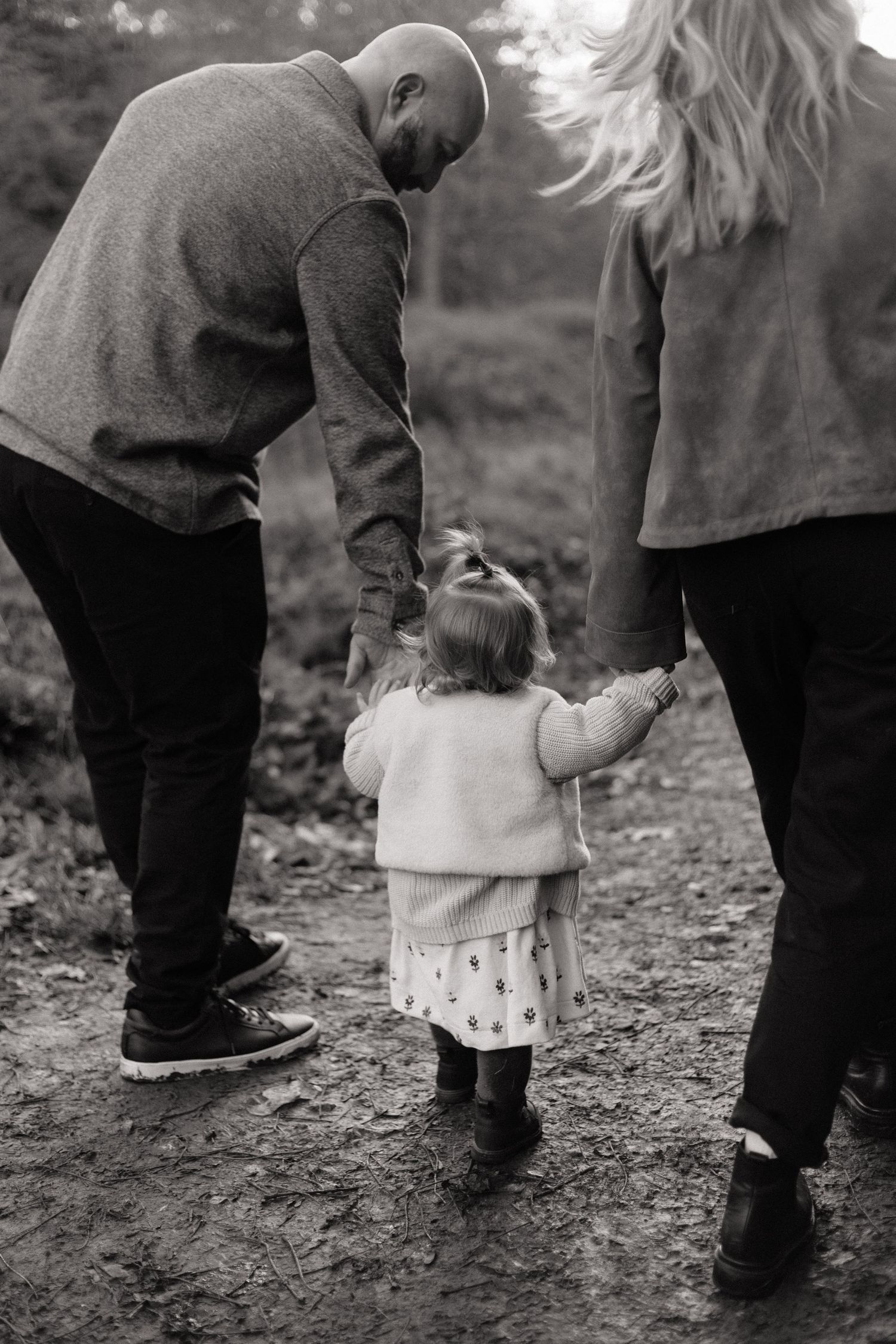 black and white photo of a mother and father  holding their toddler's hands as she walks between them