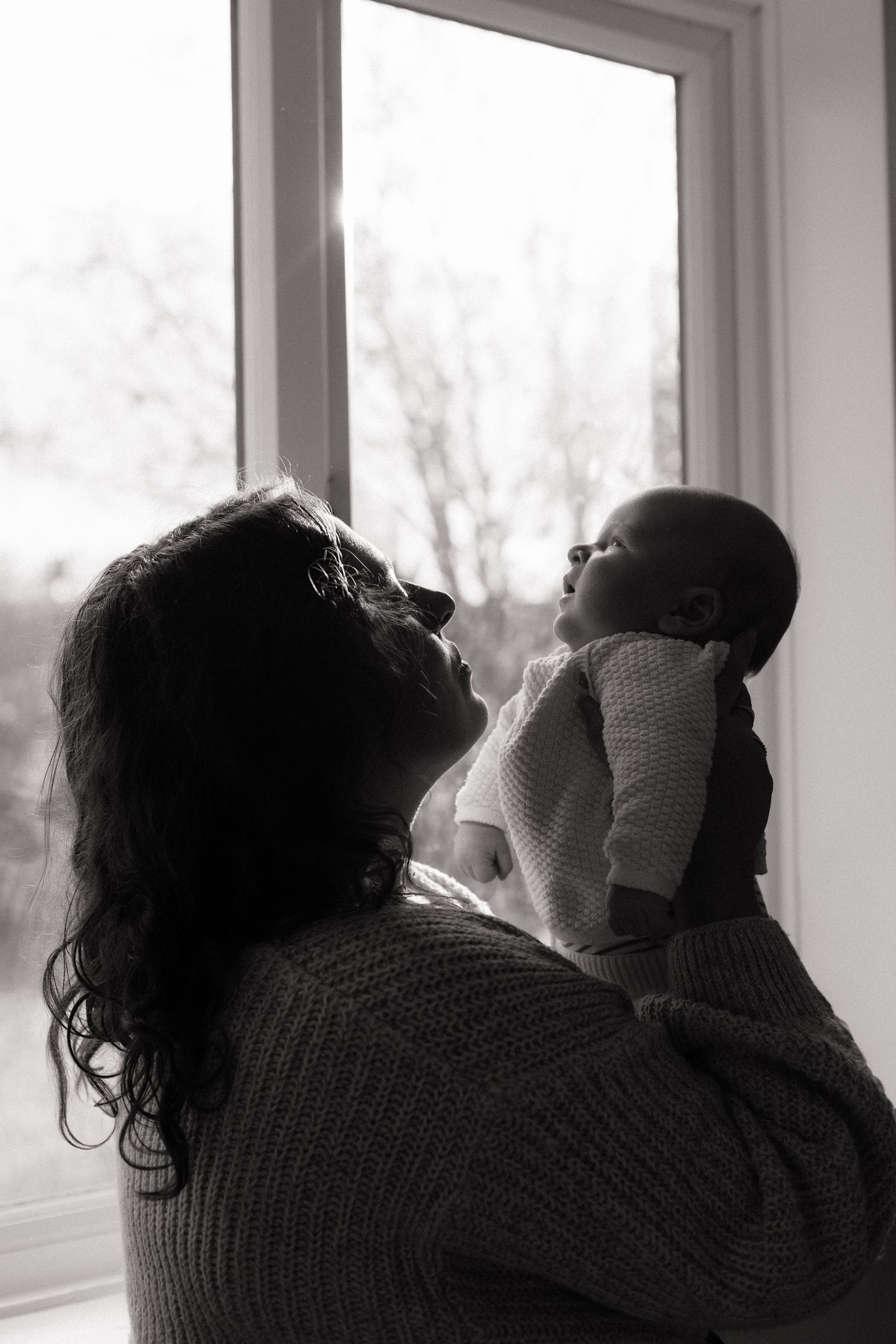 silhouette black and white photo of a mother holding up her newborn son and looking at him.