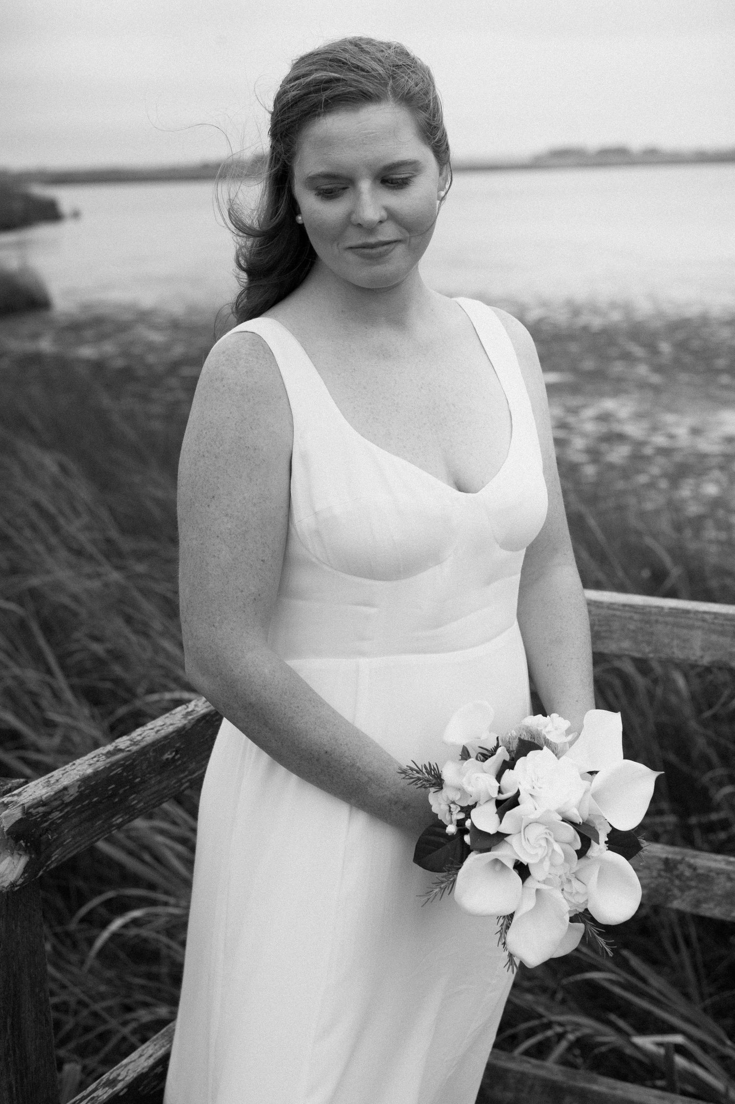 Black and white photo of bride holding classic white bouquet by coastal grasses.