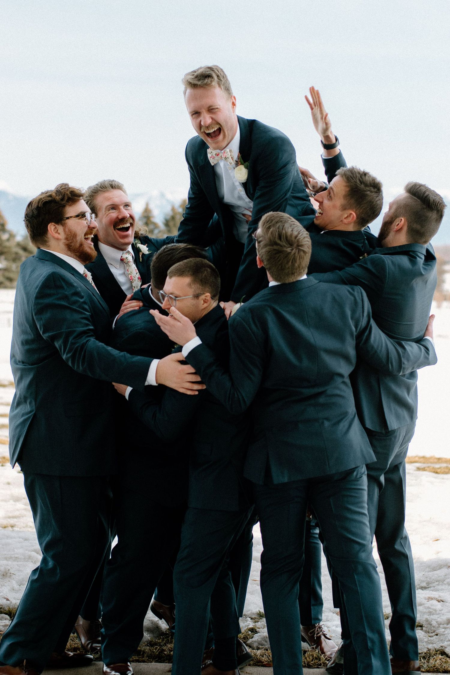 Groomsmen in dark suits sharing a joyful group celebration moment outdoors.