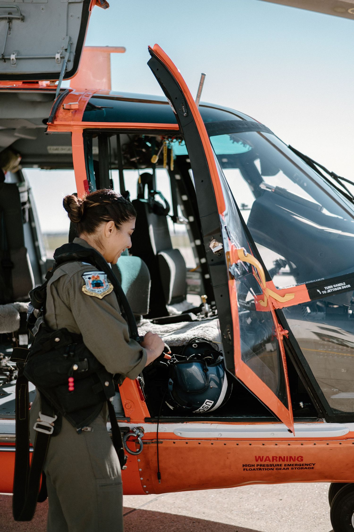 Coast Guard crew member performing pre-flight inspection on orange helicopter.