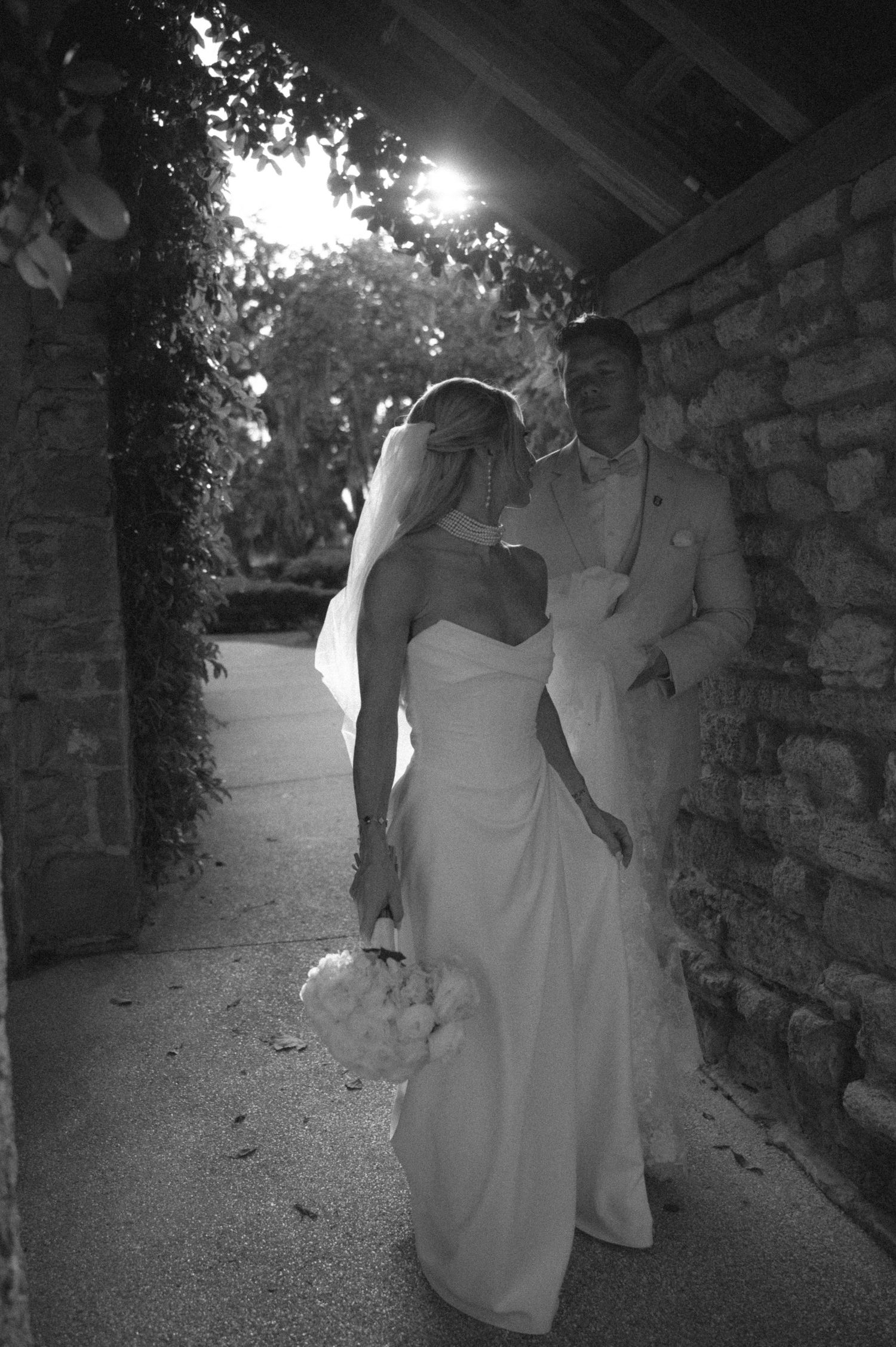 Black and white photo of bride and groom sharing a romantic moment under a covered walkway on their wedding day.
