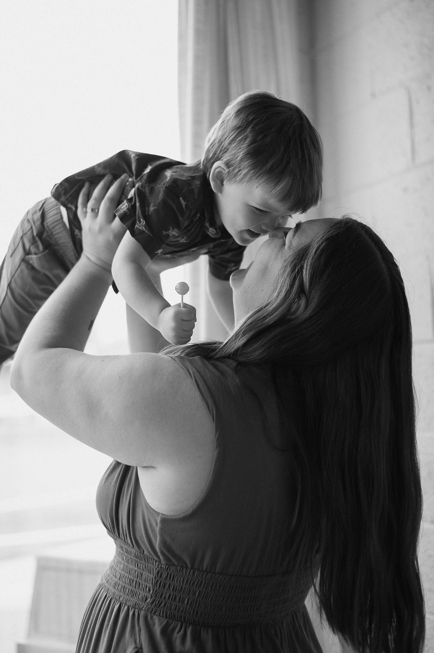 Silhouette of mother and baby dancing together by window light in intimate monochrome series.