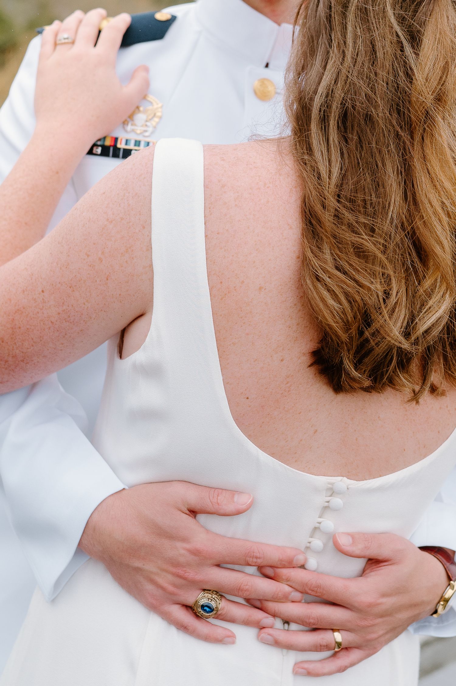 Detail shot of hands with engagement ring against white wedding dress fabric.