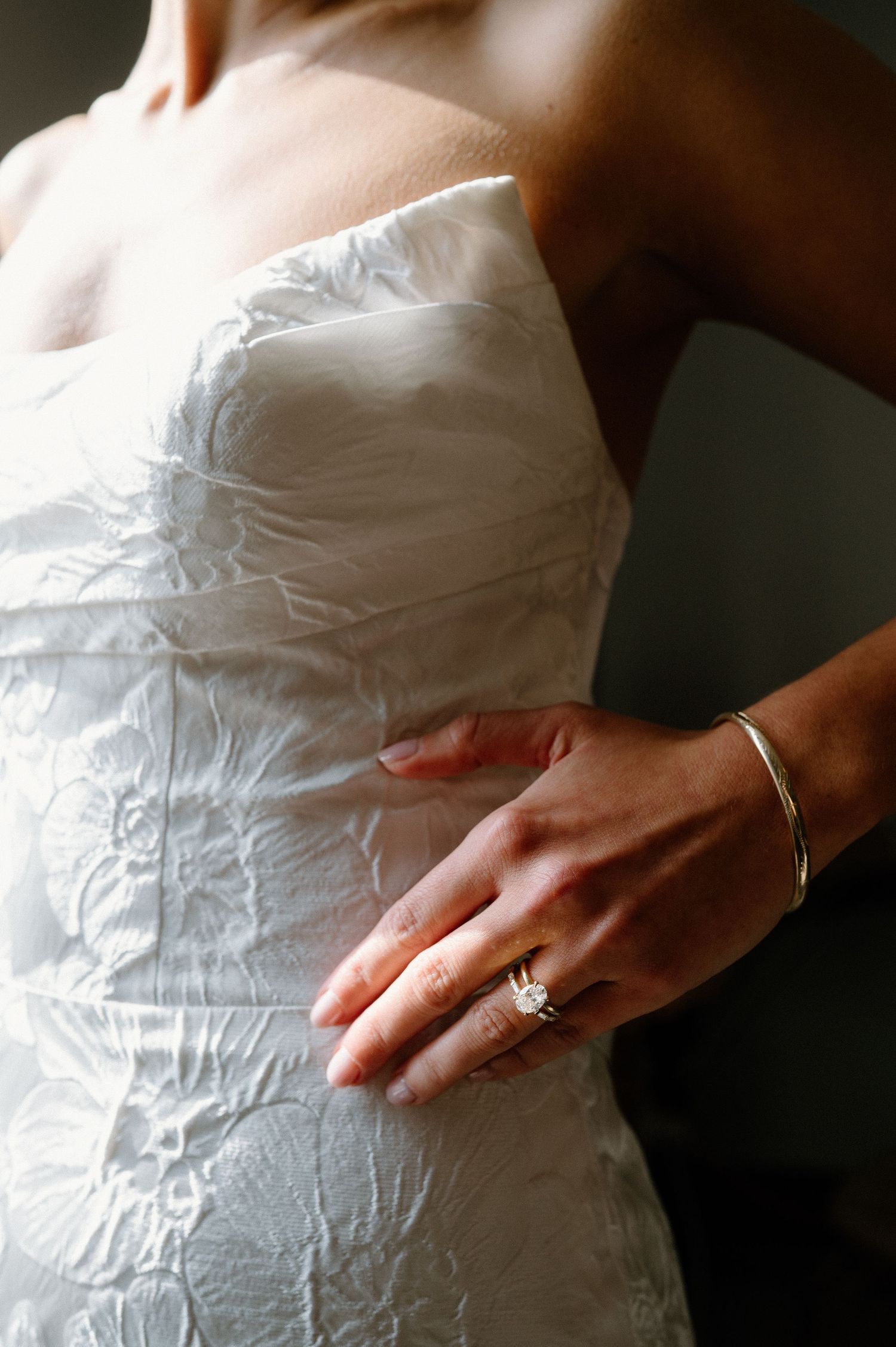 Close-up detail of a white wedding dress bodice with a diamond ring and bracelet visible on the hand.