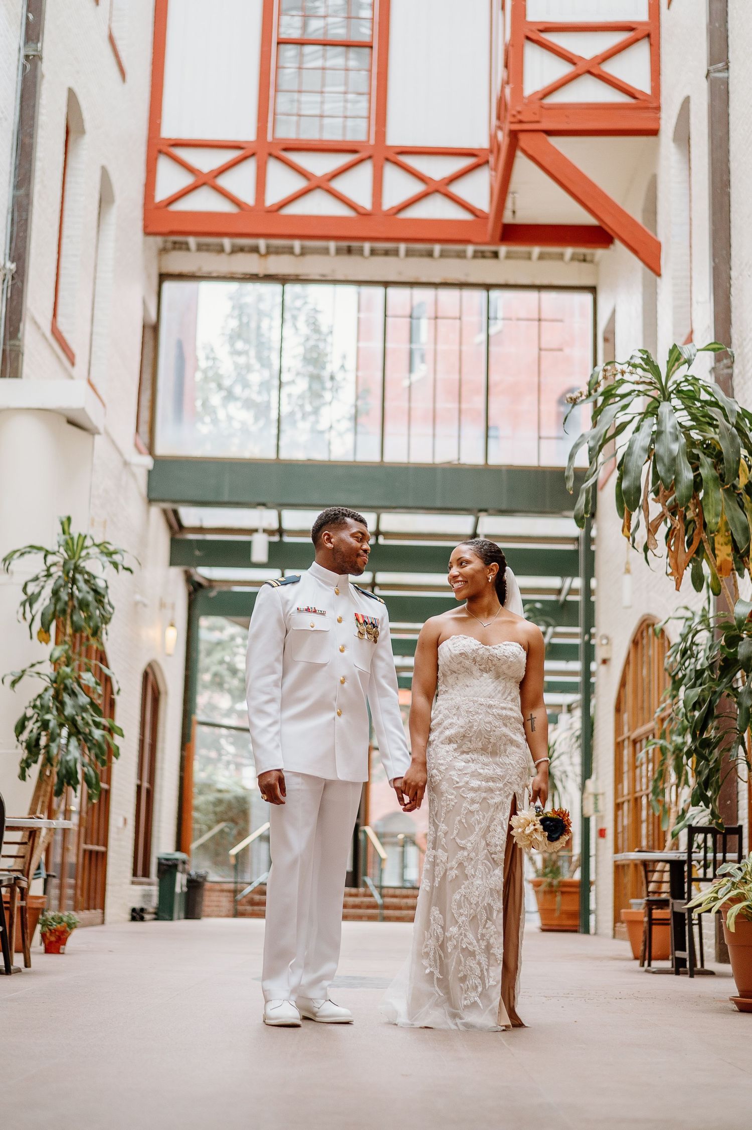 Wedding couple in white outfits walk and pose together in an elegant indoor venue with orange accents.