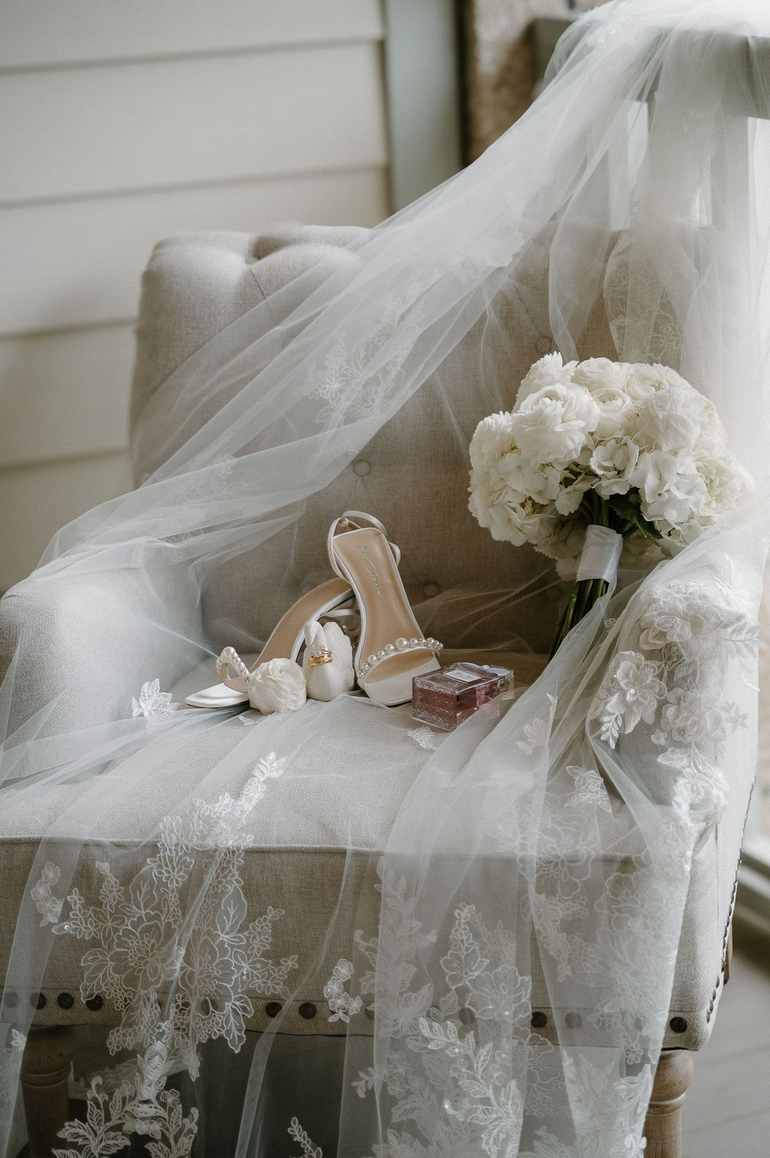 Bridal veil draped over chair with nude heeled sandals, white hydrangea bouquet, and wedding accessories.
