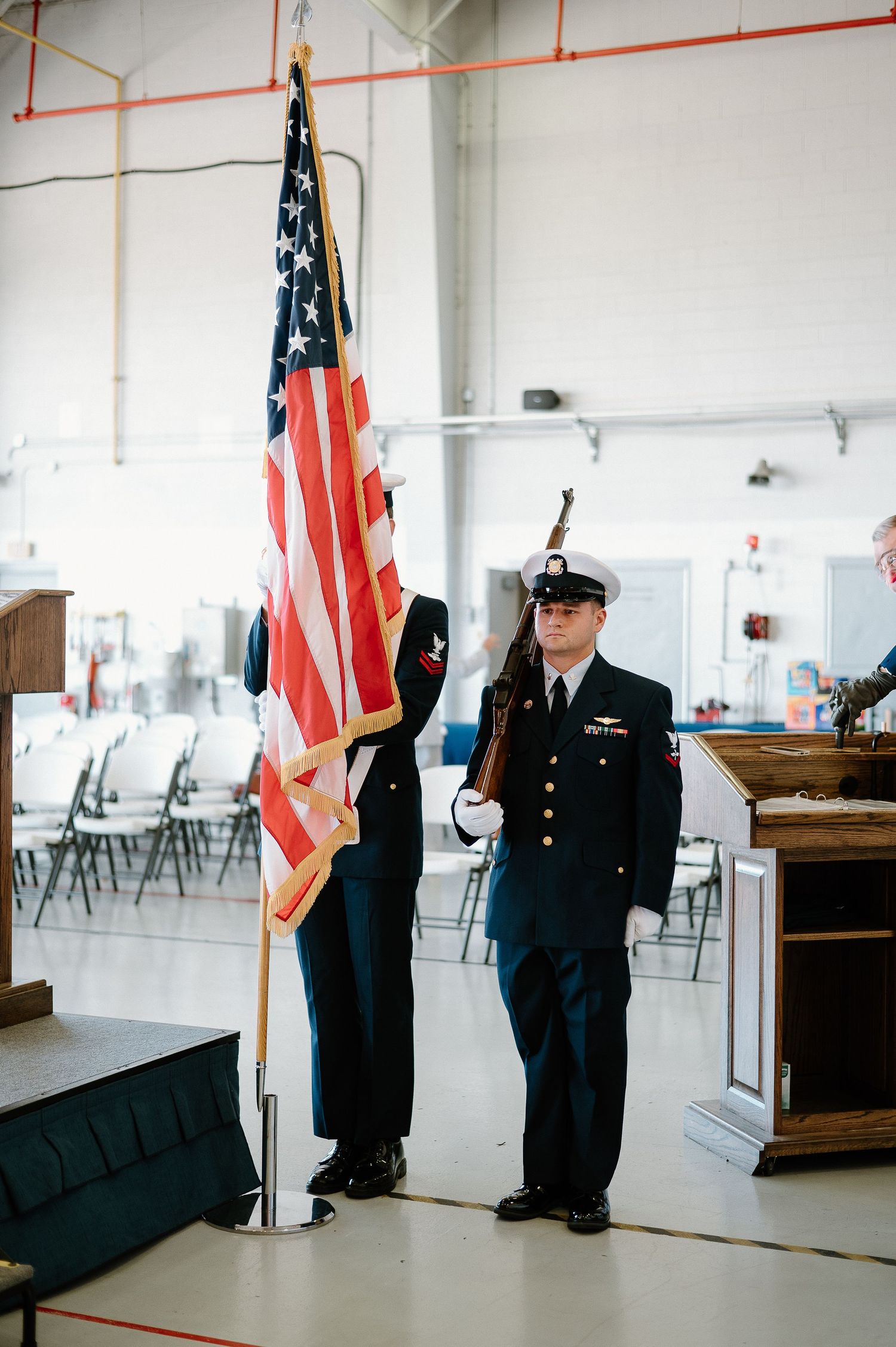 Military honor guard members standing at attention with American flags in ceremony hall.
