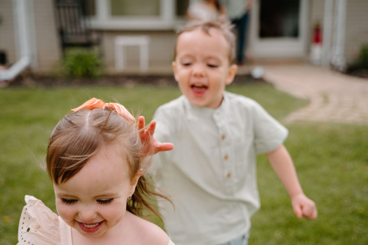 Two happy toddlers running and playing outdoors in a backyard on a sunny day.
