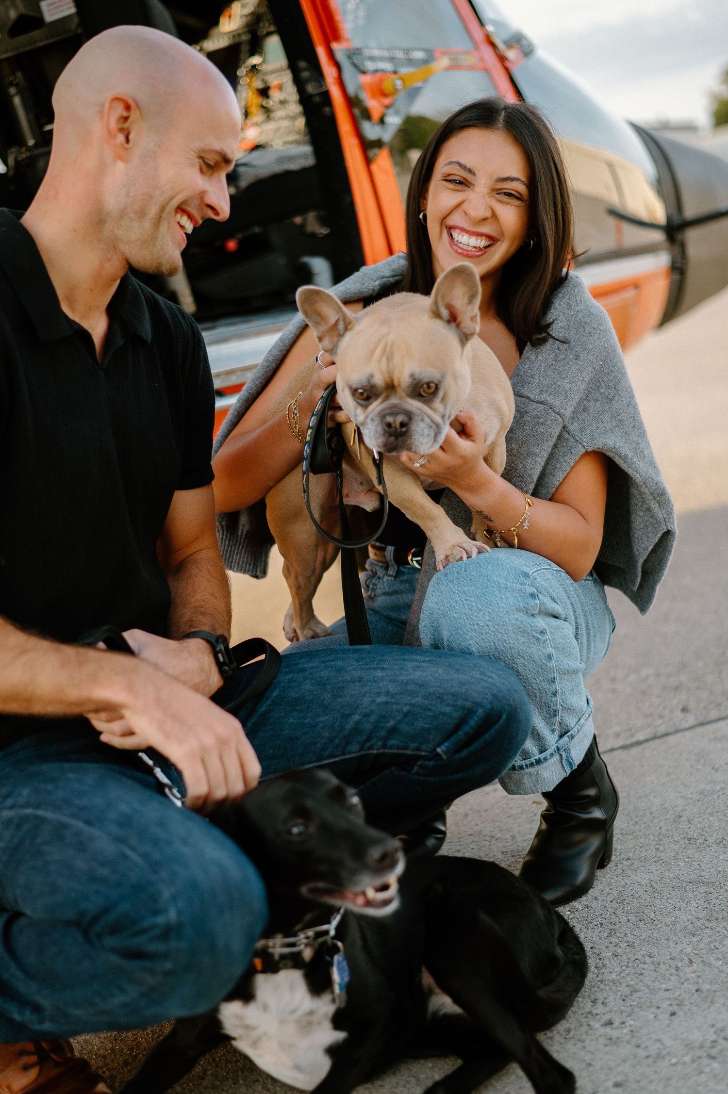Happy couple plays with their dogs near helicopter during sunset photoshoot.