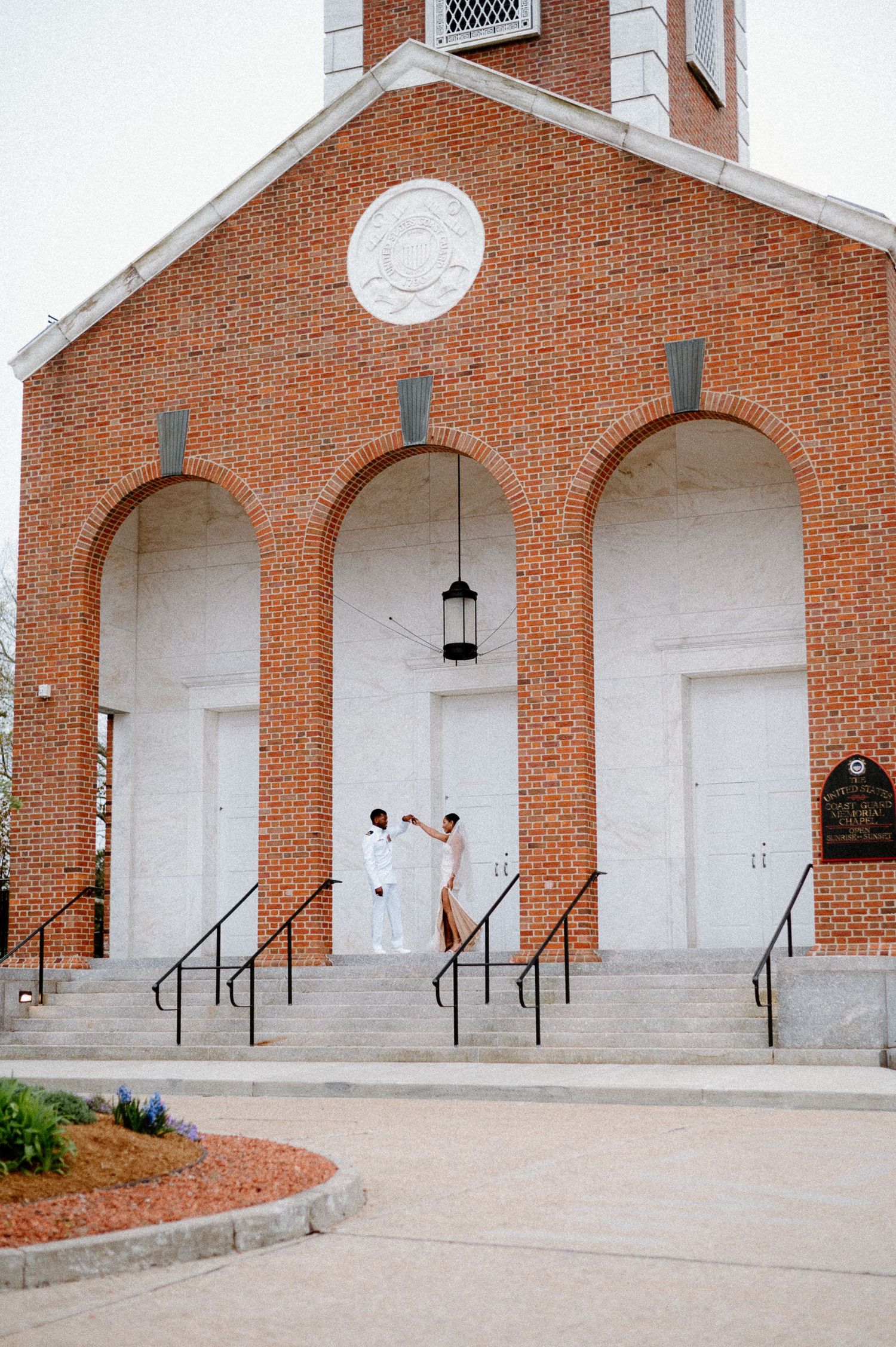 Exterior view of a red brick church with white arched doorways and steps.