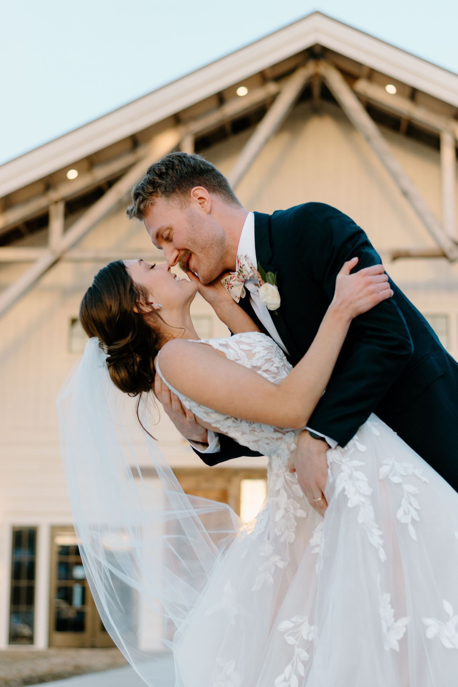 Elegant wedding scene against a white barn backdrop during sunset.