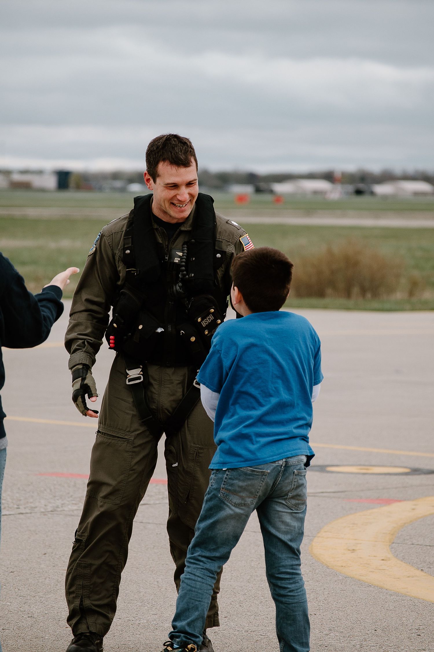 A Coast Guard pilot in flight suit interacting with visitors on the tarmac.