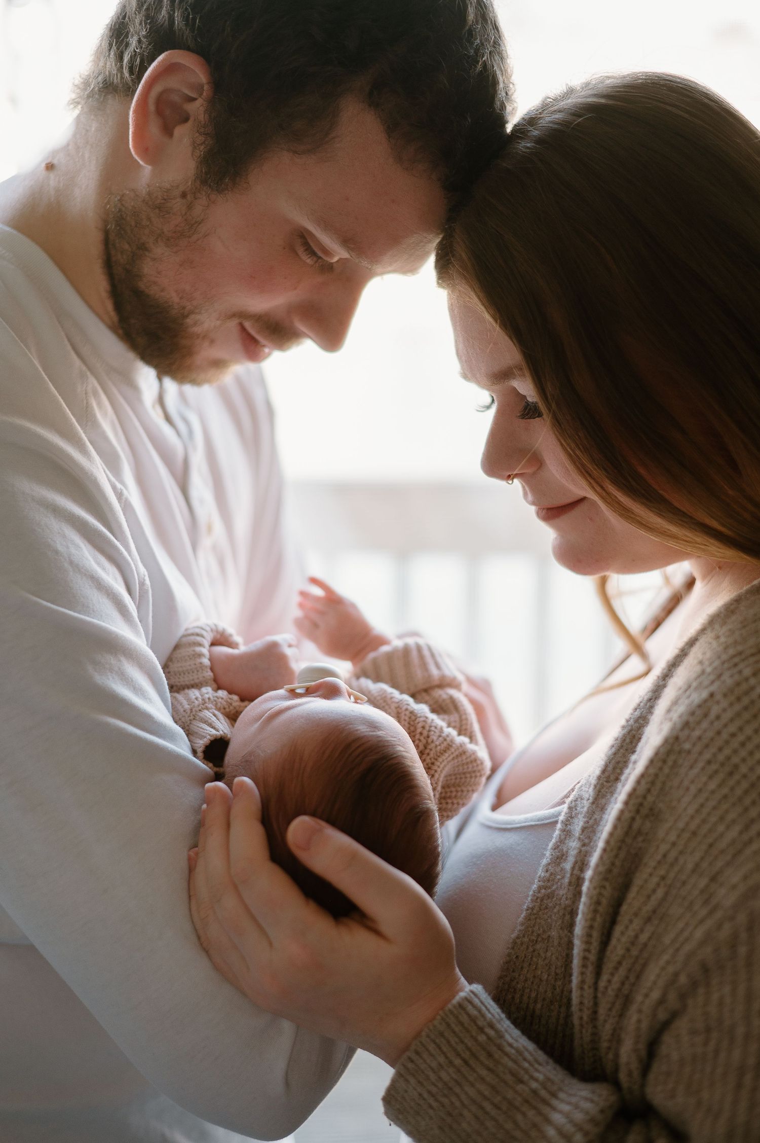 Close-up images of new parents tenderly bonding with their newborn baby in soft natural light.