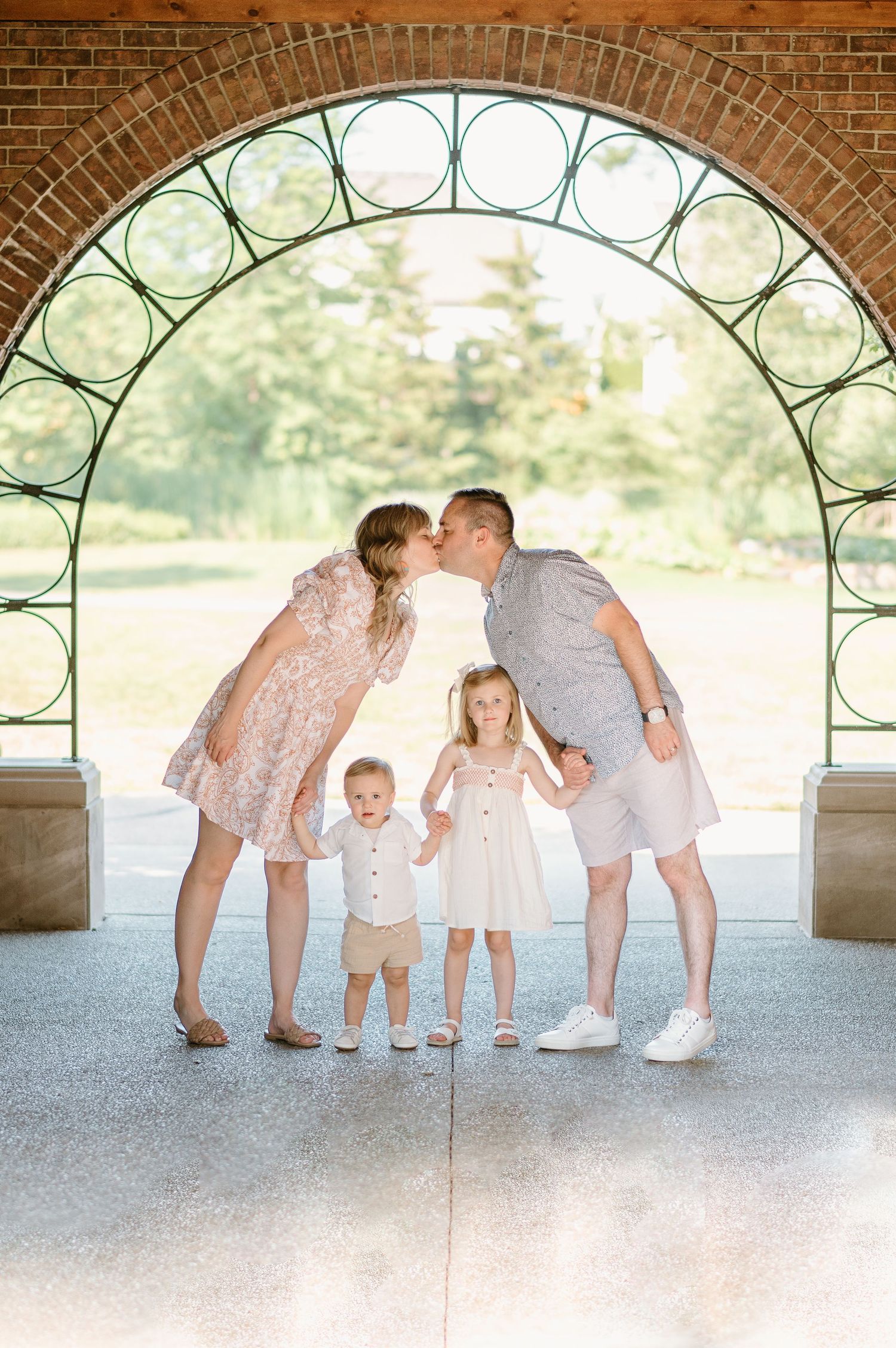 Family poses under a decorative brick archway sharing a tender moment together.