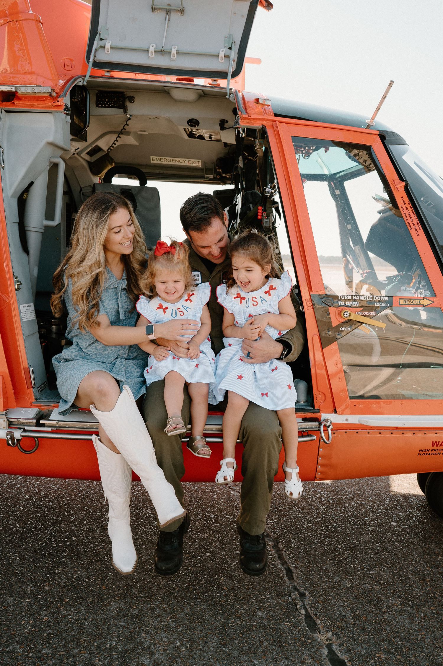 Family of four sitting in an orange helicopter, two young girls in matching USA dresses with parents smiling.
