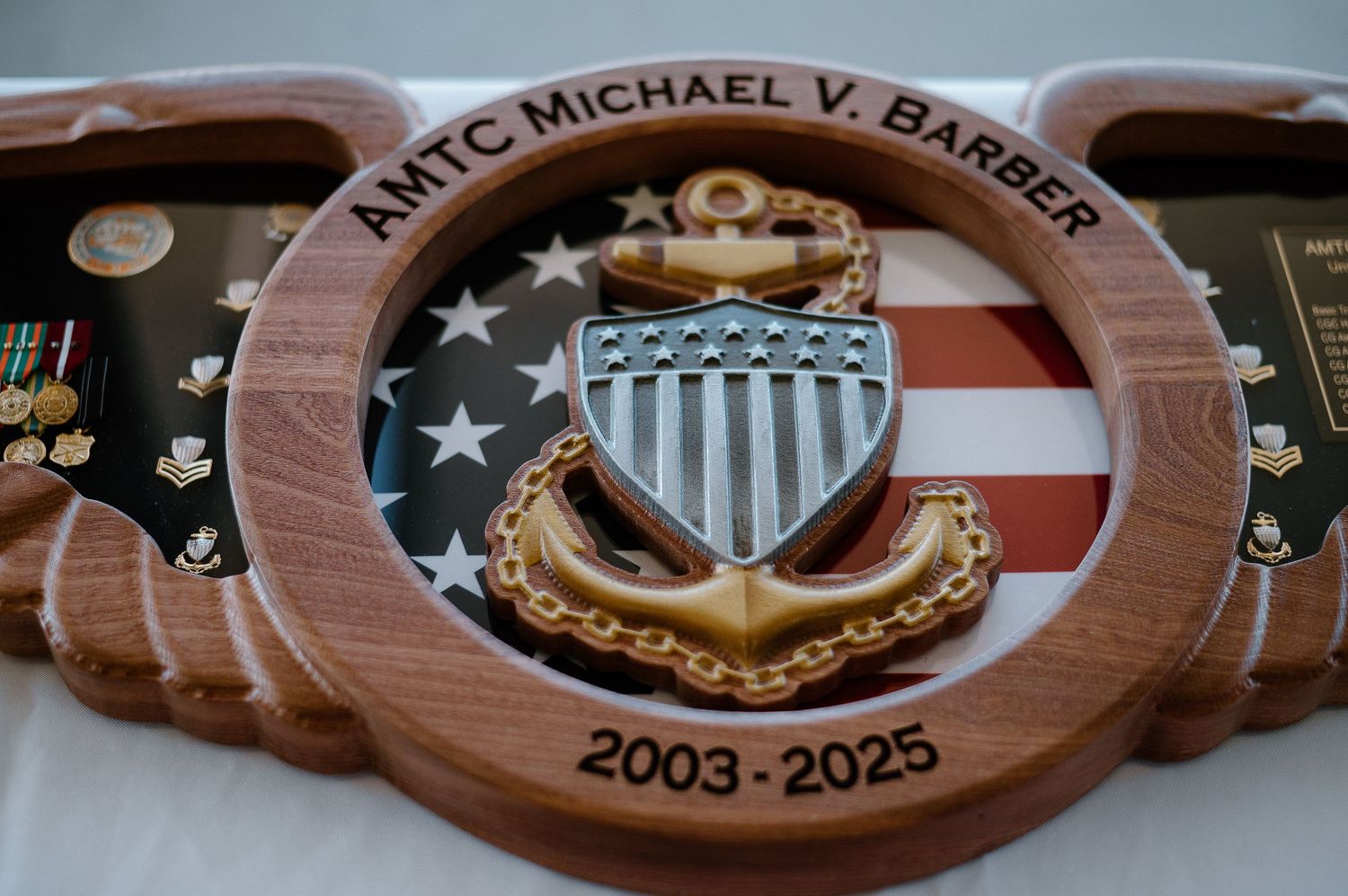 Wooden ceremonial plaque with military insignias and dates displayed against dark background.