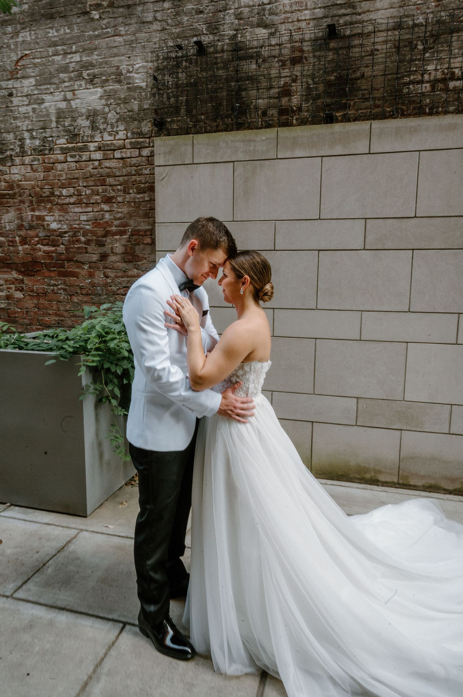 Romantic wedding couple embracing against a rustic brick wall backdrop.