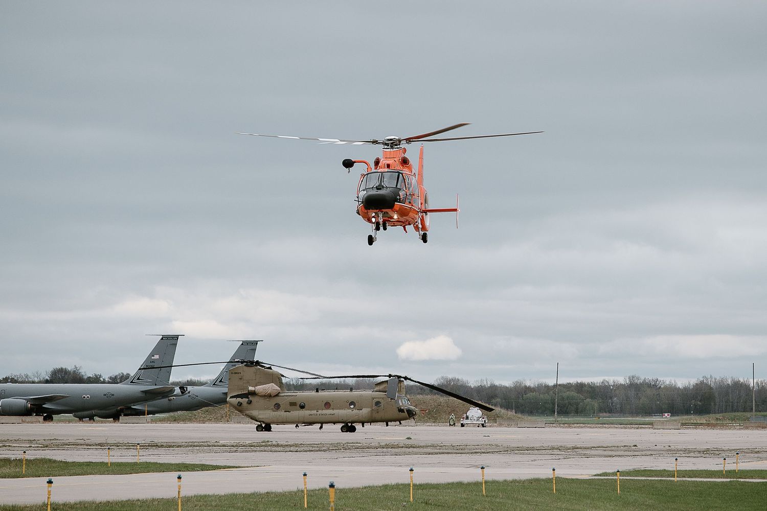 Military helicopters lined up on an airfield under cloudy skies.