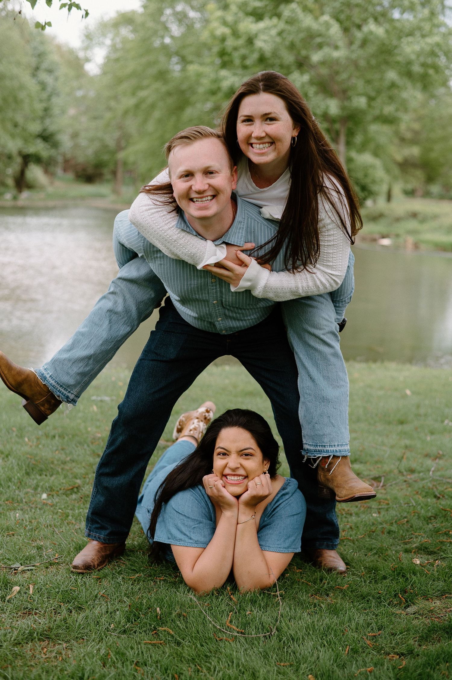 Three people pose playfully in a park setting creating a human pyramid.