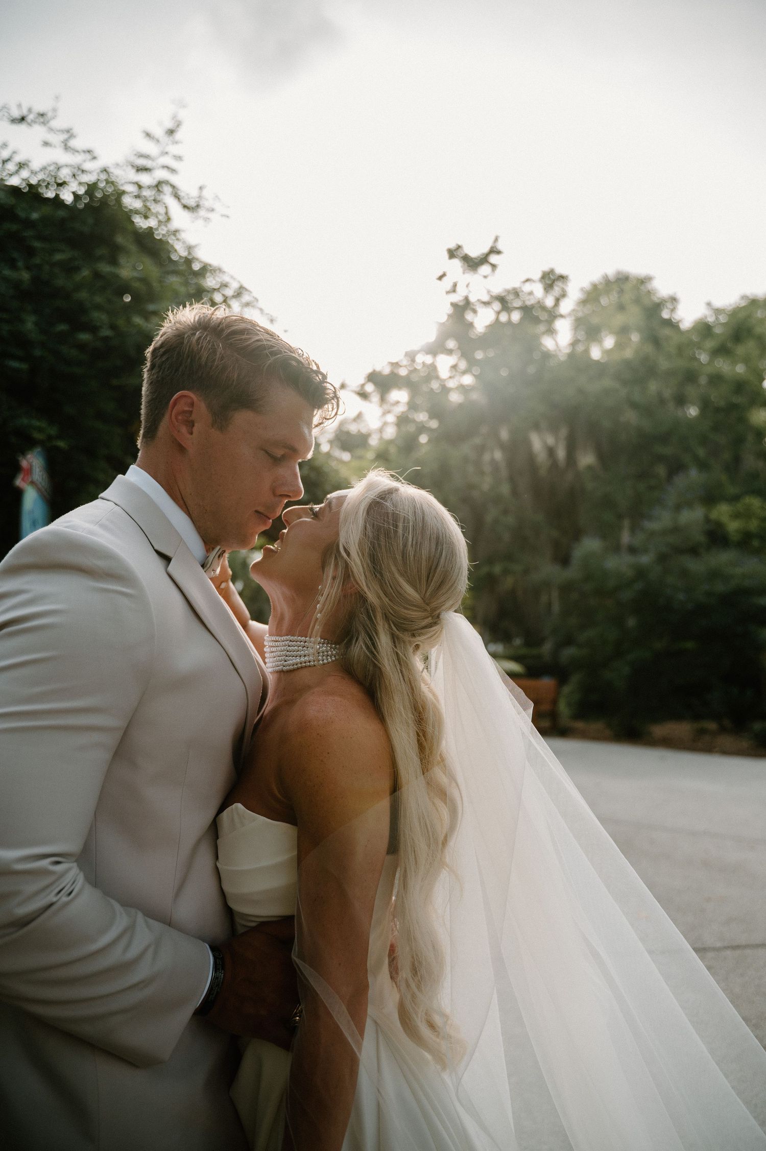 A bride and groom share an intimate moment, nearly kissing outdoors, with the bride in a white gown and veil.