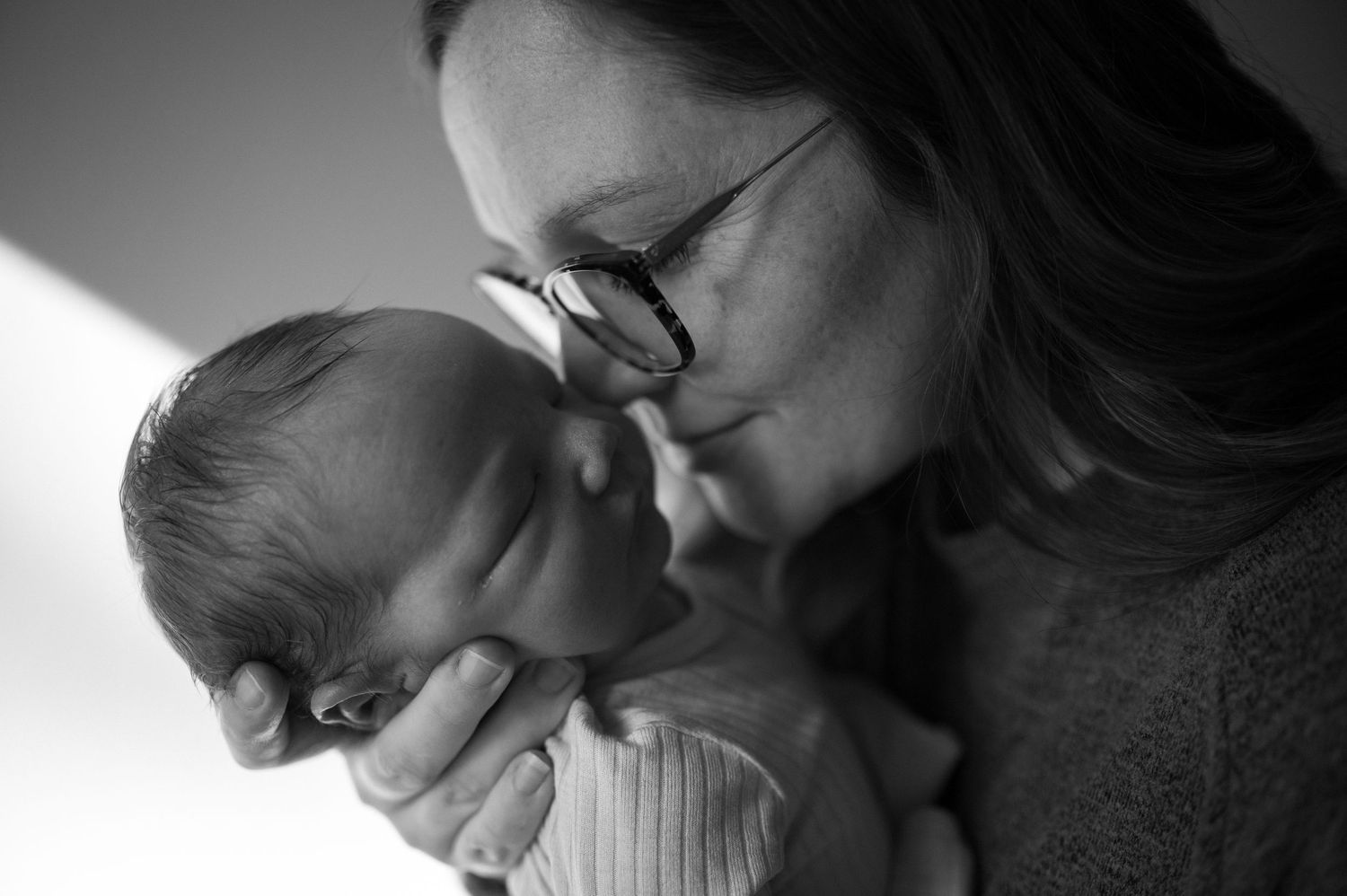 Black and white photo of a mother tenderly kissing her newborn baby while cradling it gently in her hands.