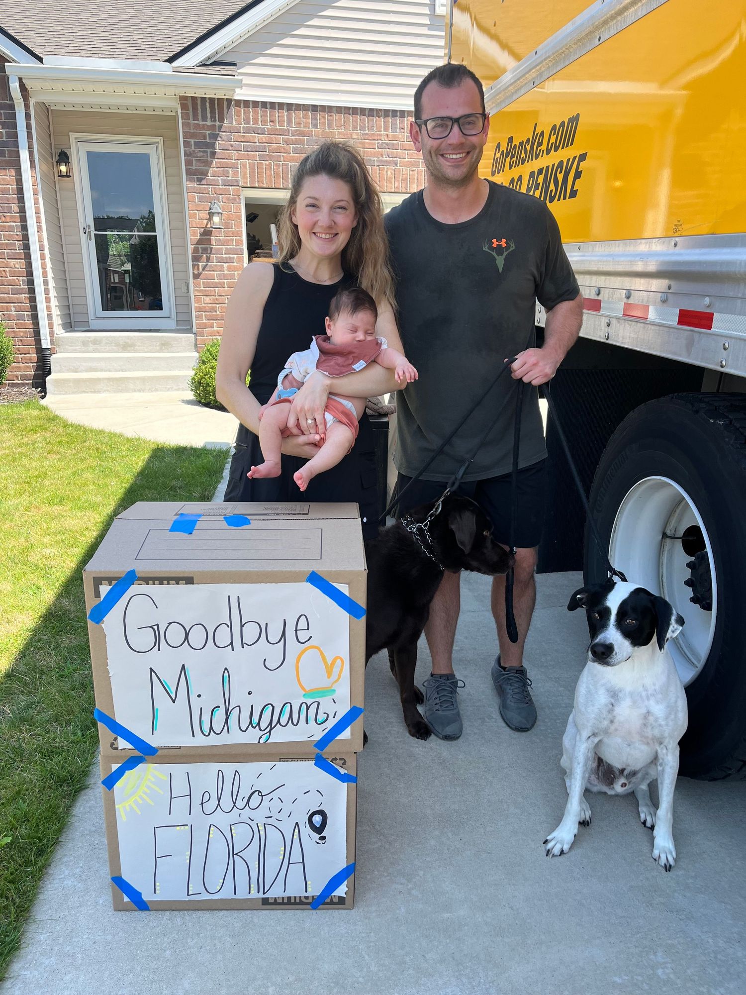 Family with dog holds signs showing their move from Michigan to Florida in driveway series.