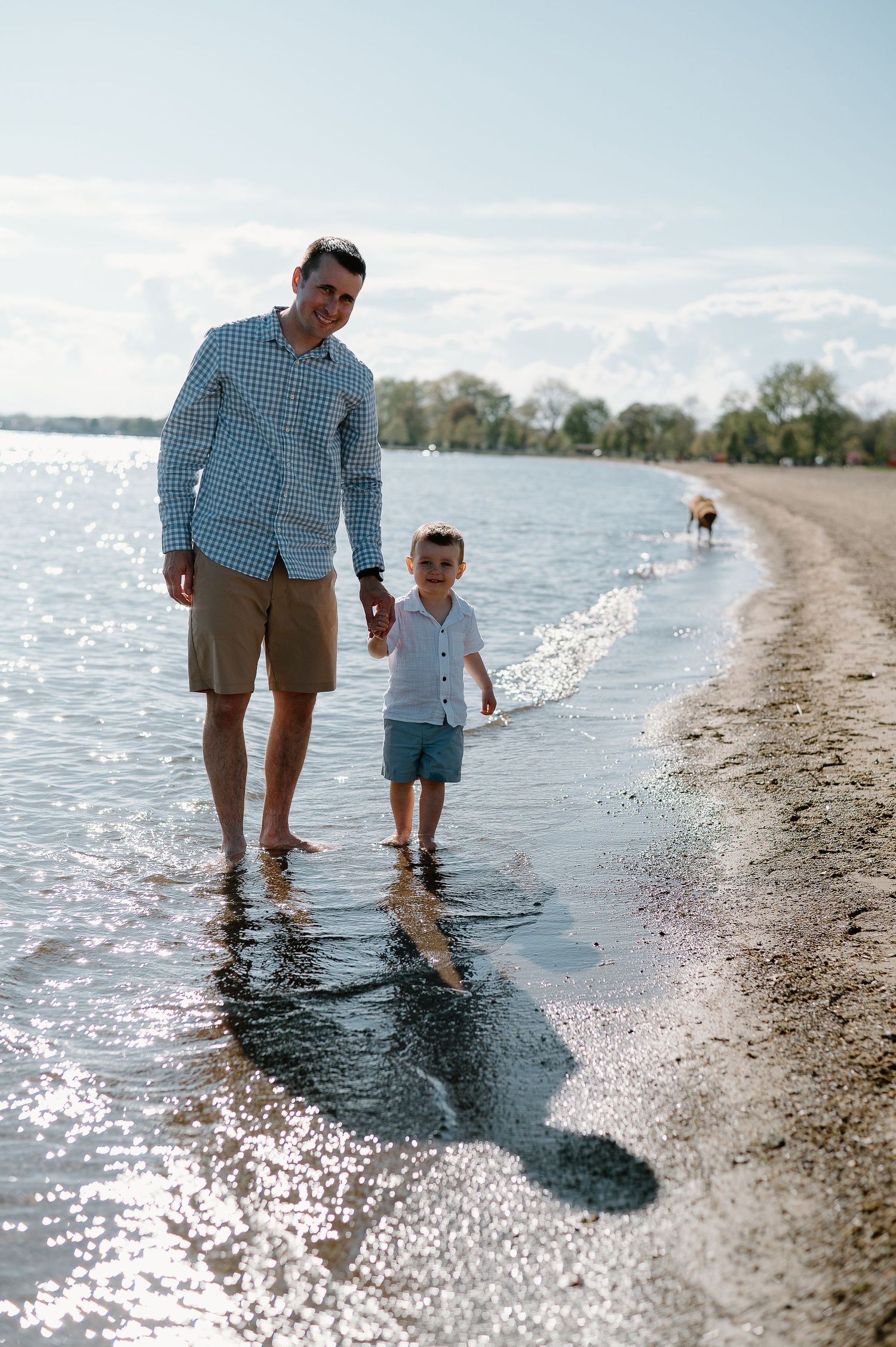 Parent and child walking along the water's edge on a bright sunny beach day.