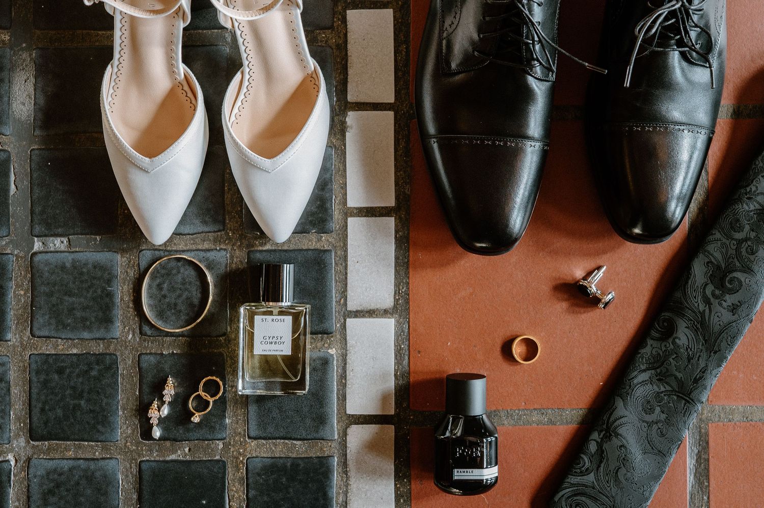 Wedding accessories including white bridal shoes, rings, and black formal shoes arranged on tiled and leather surfaces.