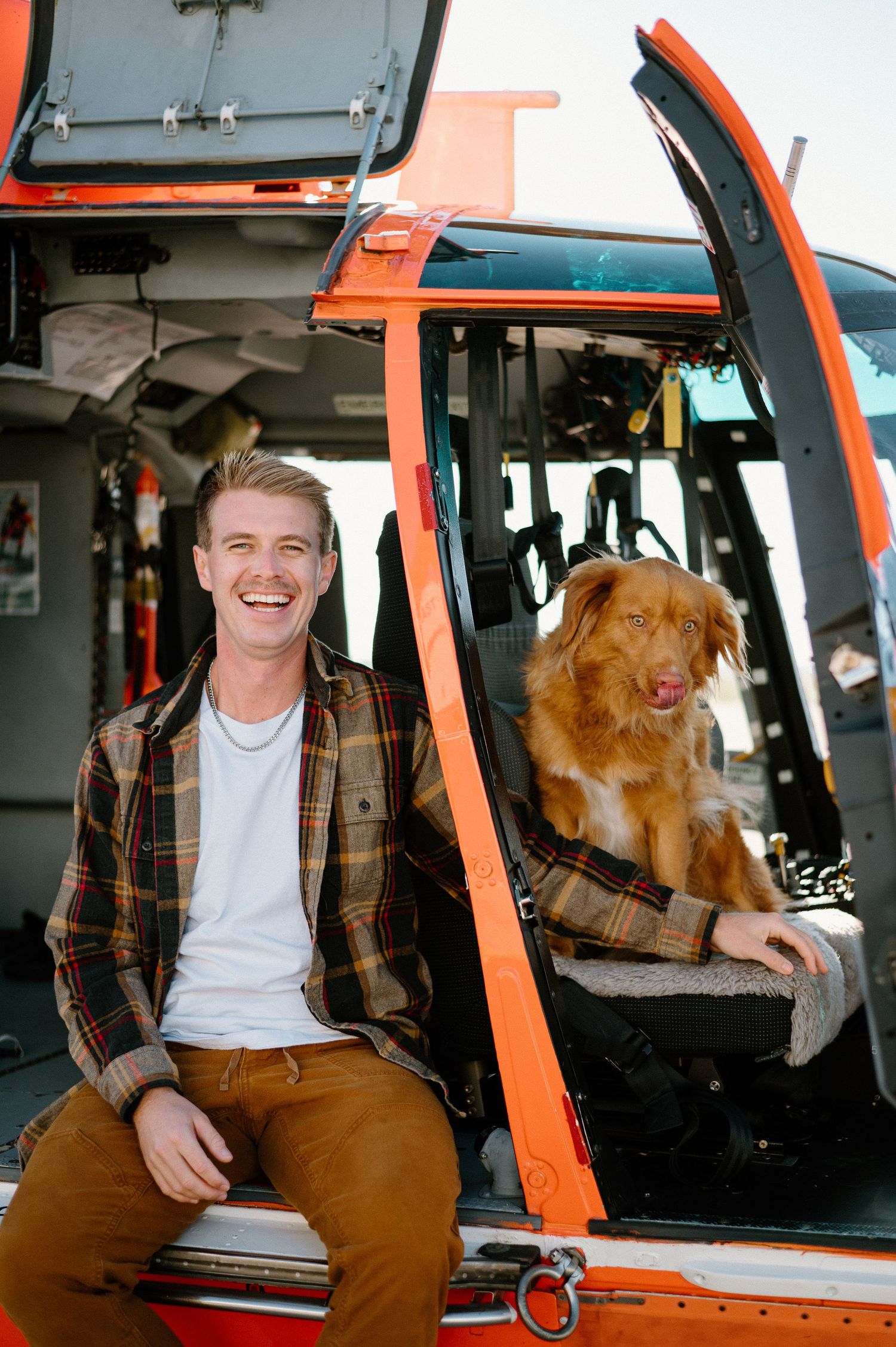 Golden retriever and companion pose together in orange helicopter cockpit during photoshoot.