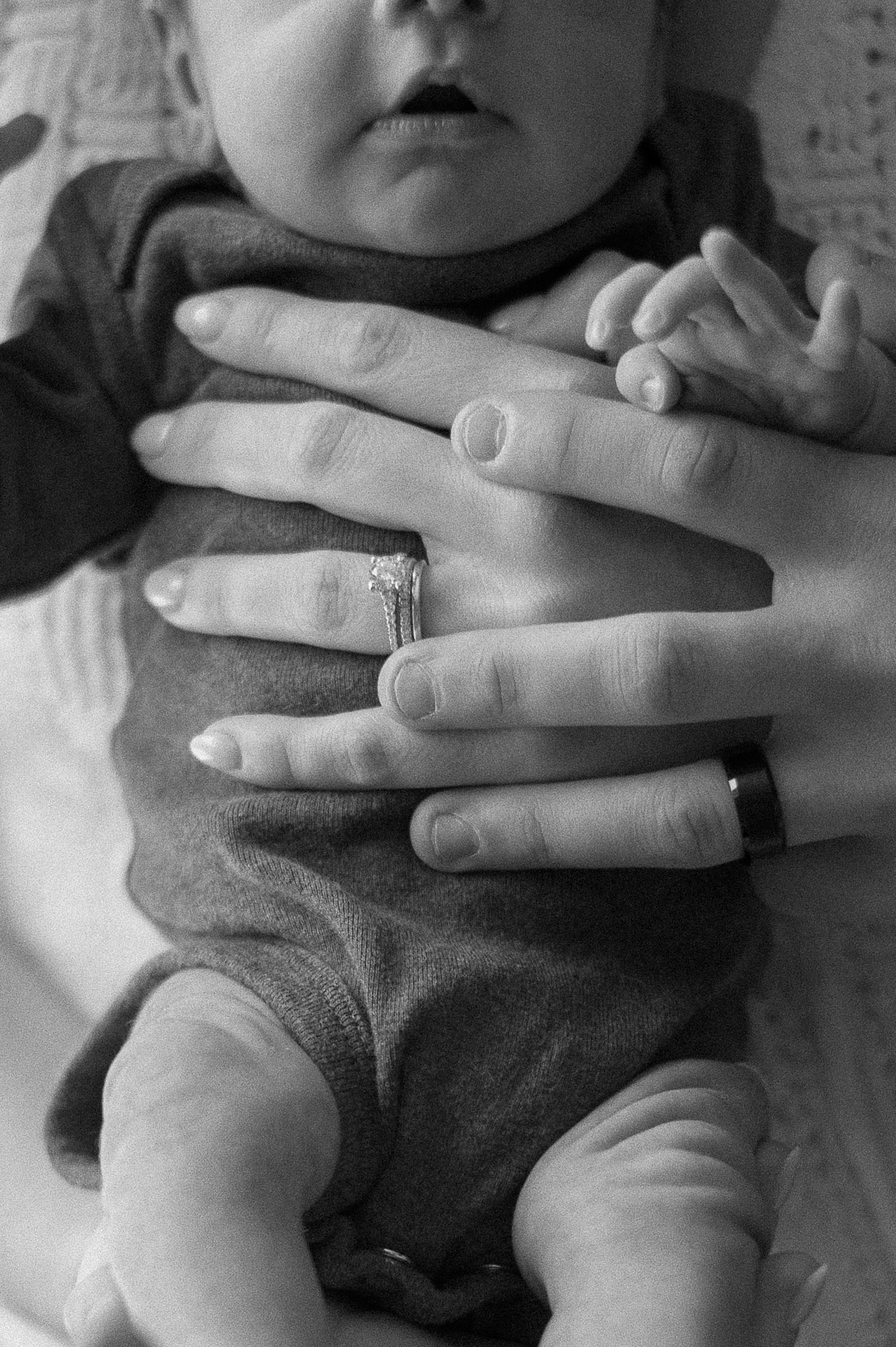 Close-up black and white image of wedding rings with baby hands.