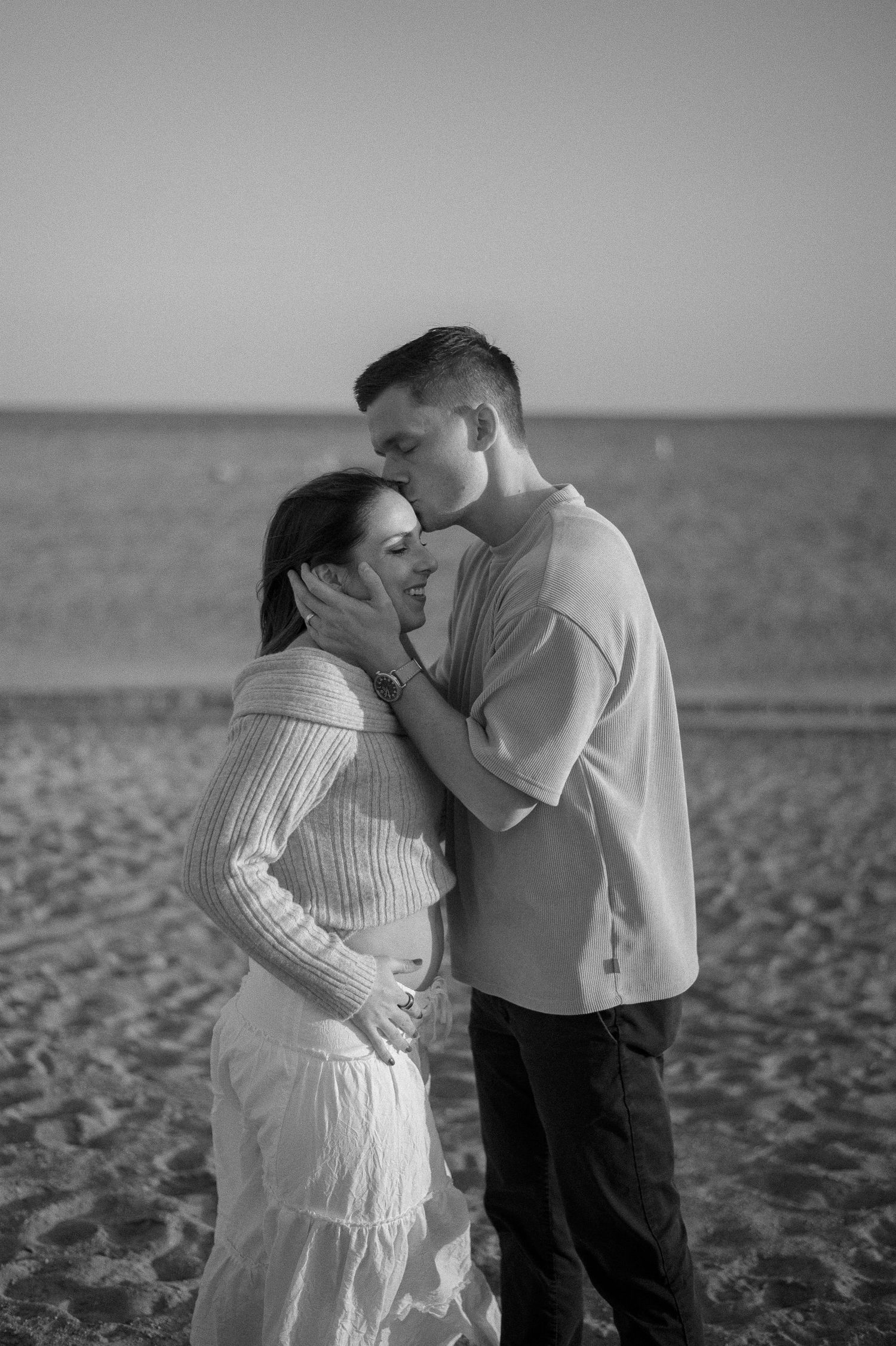 An intimate black and white portrait of a couple on a sandy beach.