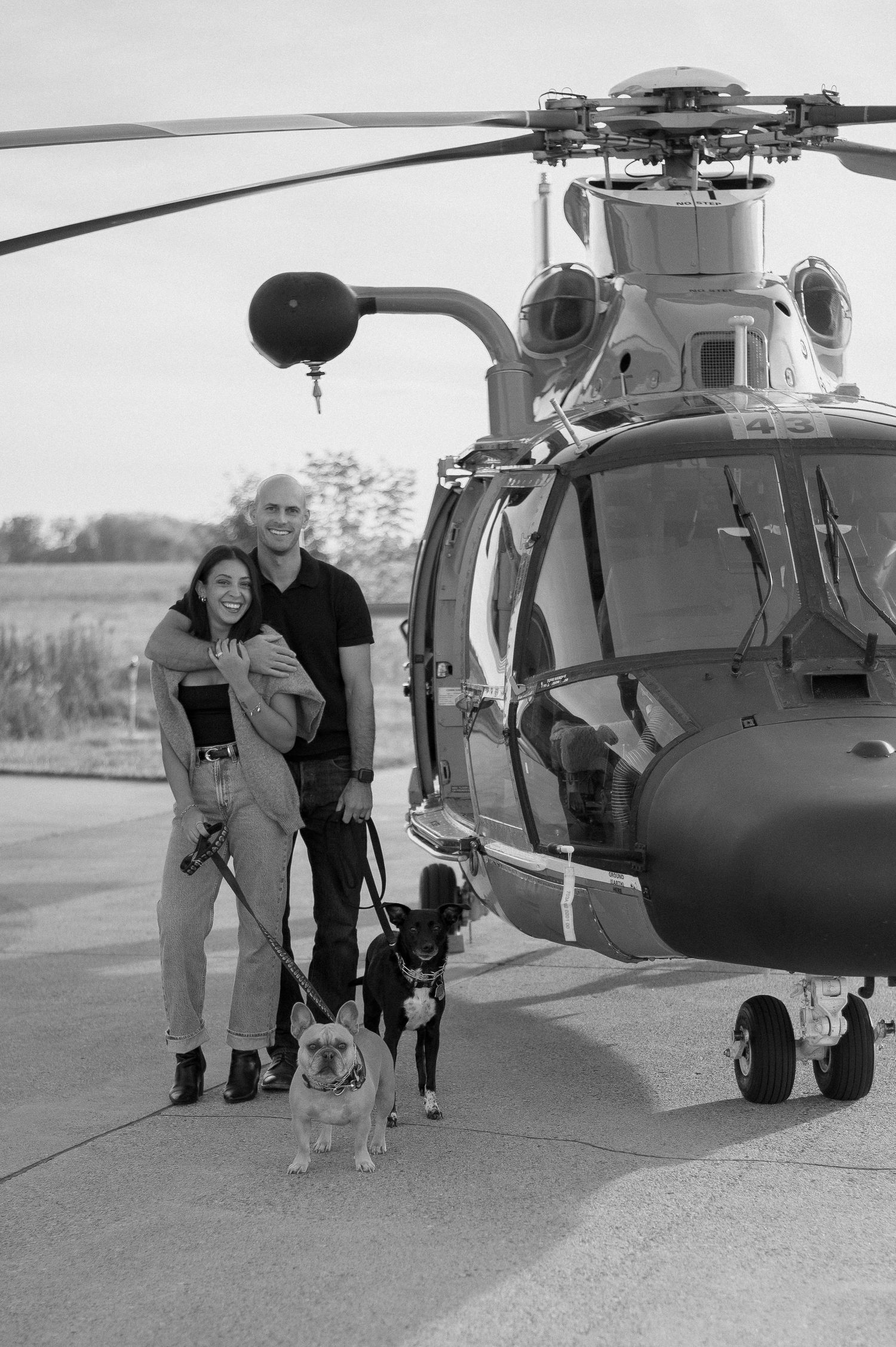 Black and white photo of people and dogs standing near military helicopter.