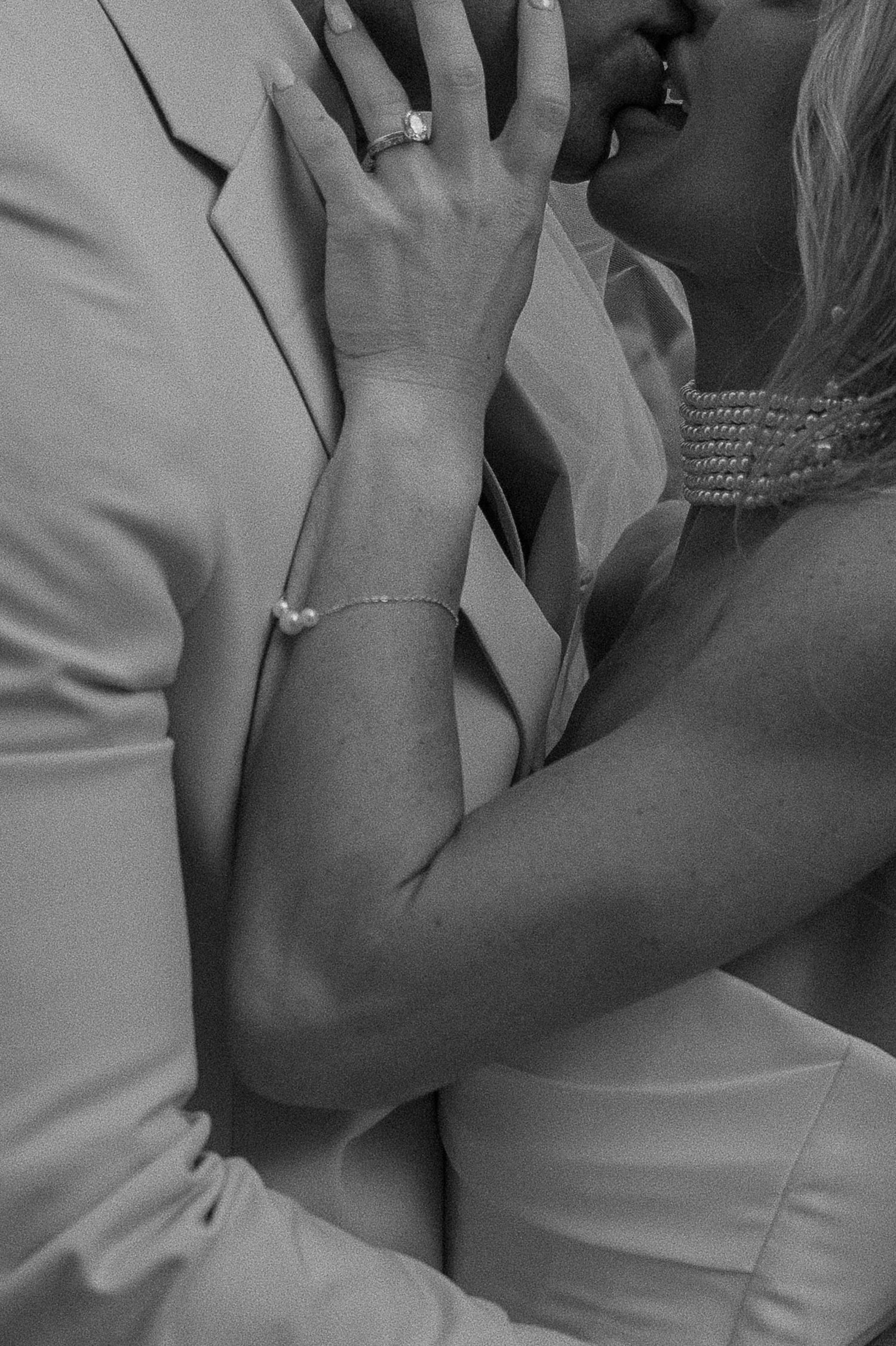 Black and white photo of a couple kissing, bride wearing a ring and bracelet embracing groom in a suit.