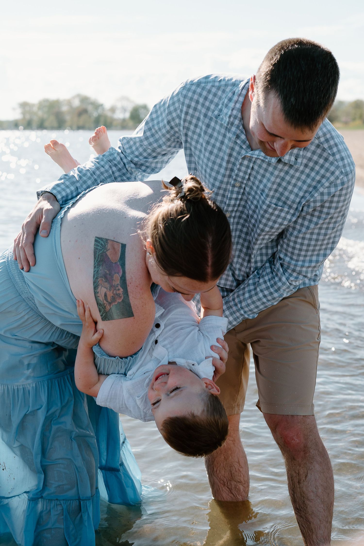 Family shares playful moments and laughter at the water's edge on a sunny beach.