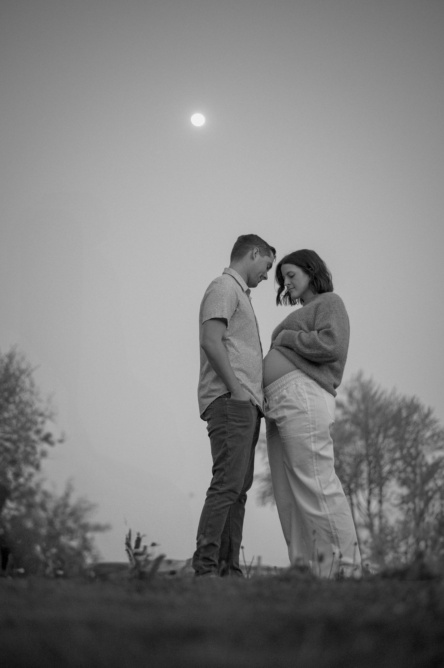 Black and white romantic portraits taken against a moody sky at dusk.