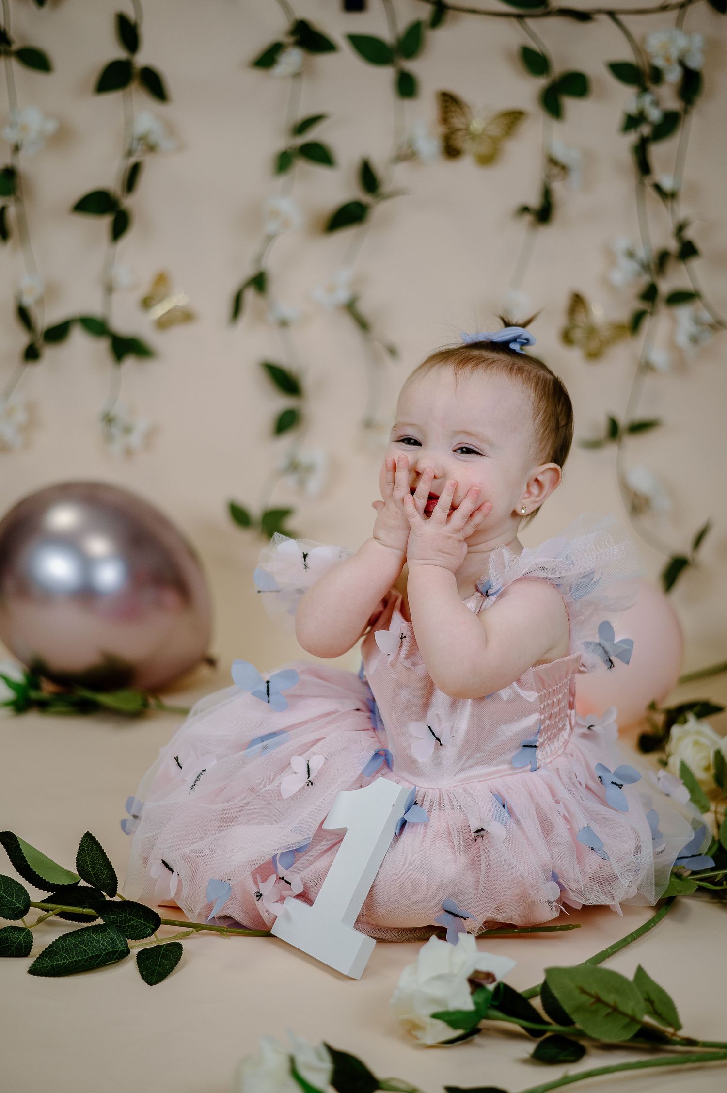 Baby in pink dress plays with decorative butterflies during milestone photo session.