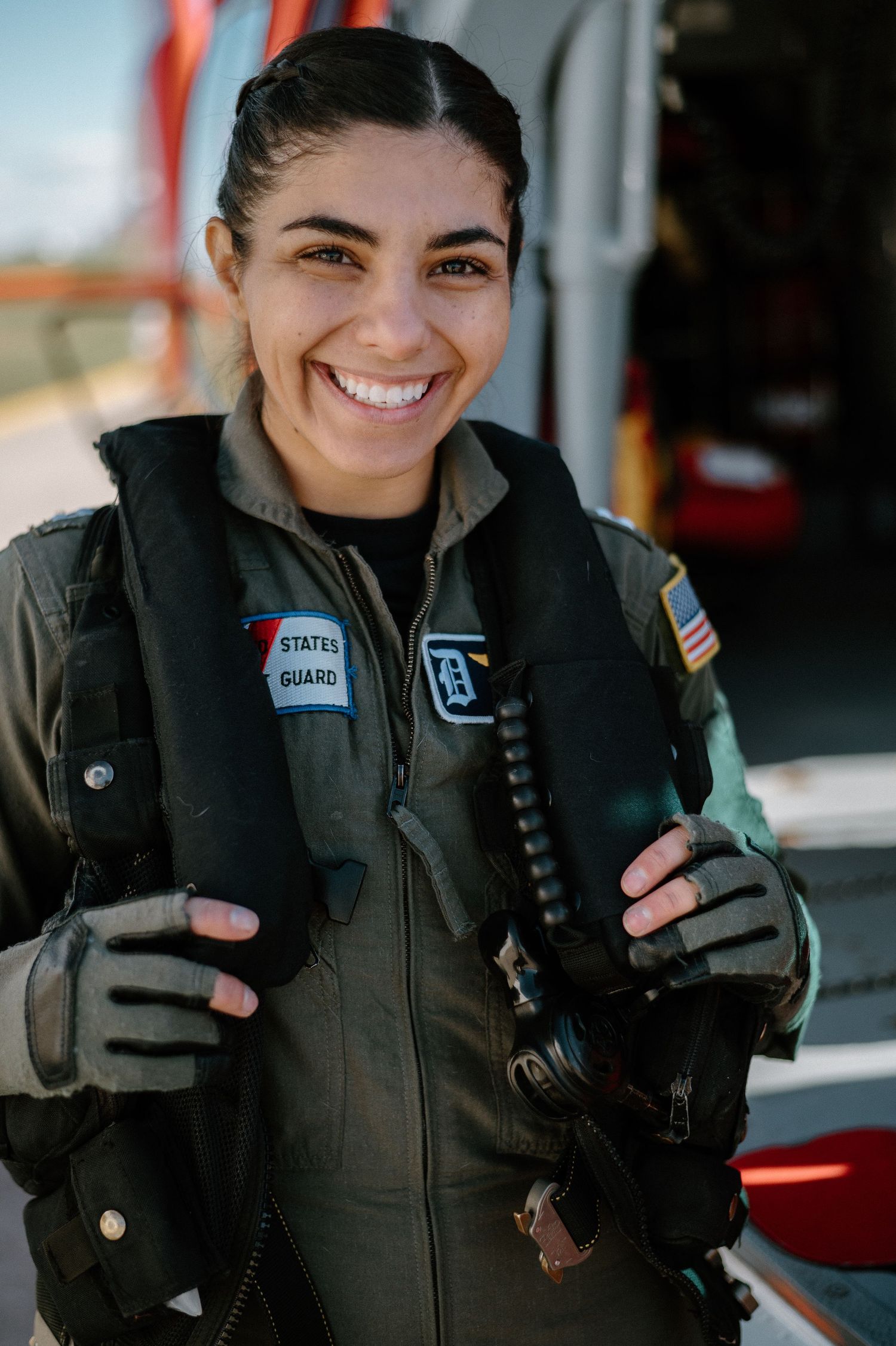 Coast Guard pilot in flight gear smiling while holding equipment.